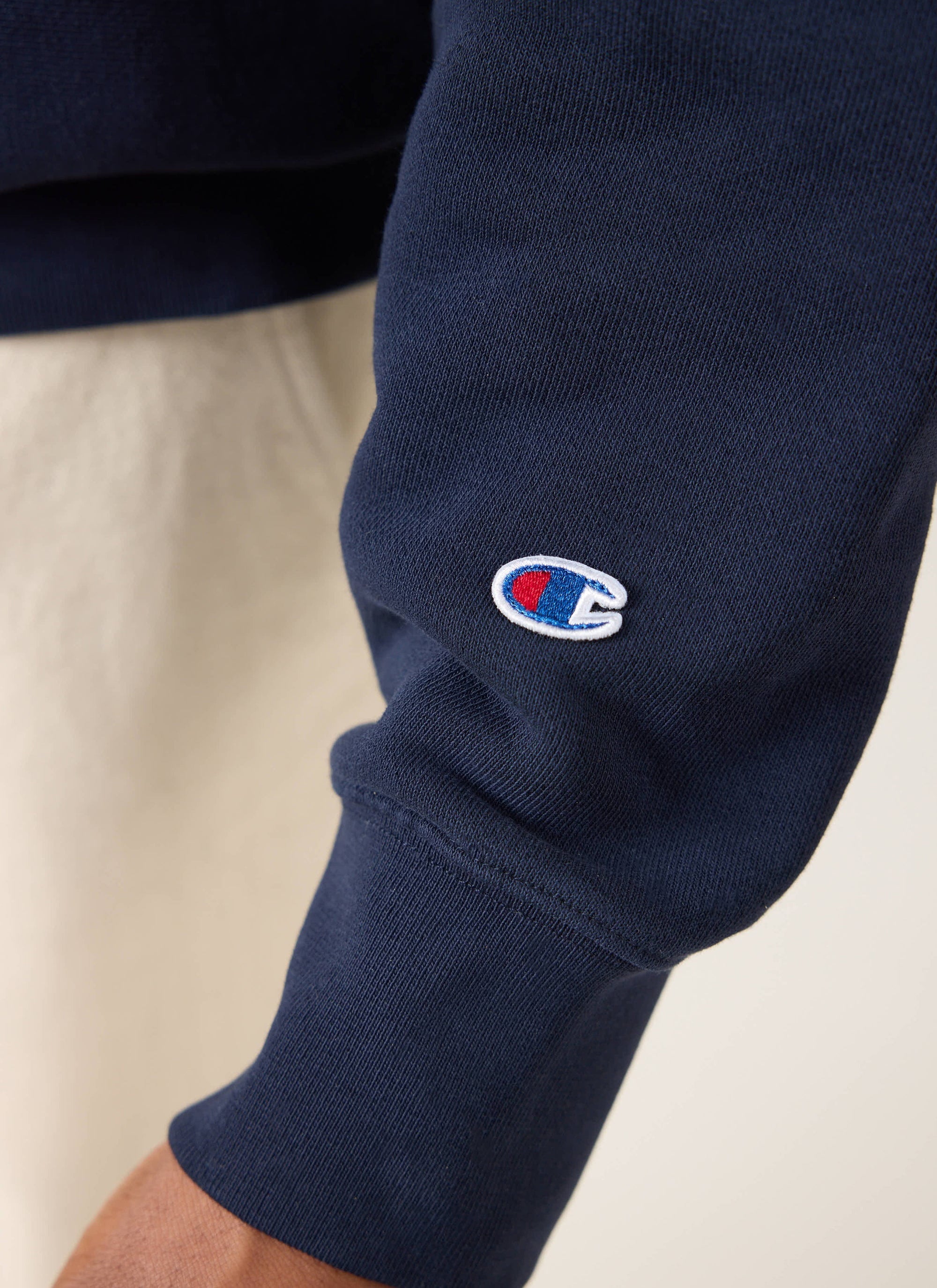 A close-up of the embroidered Champion logo on the sleeve of the navy Champion x Percival jersey sweatshirt.