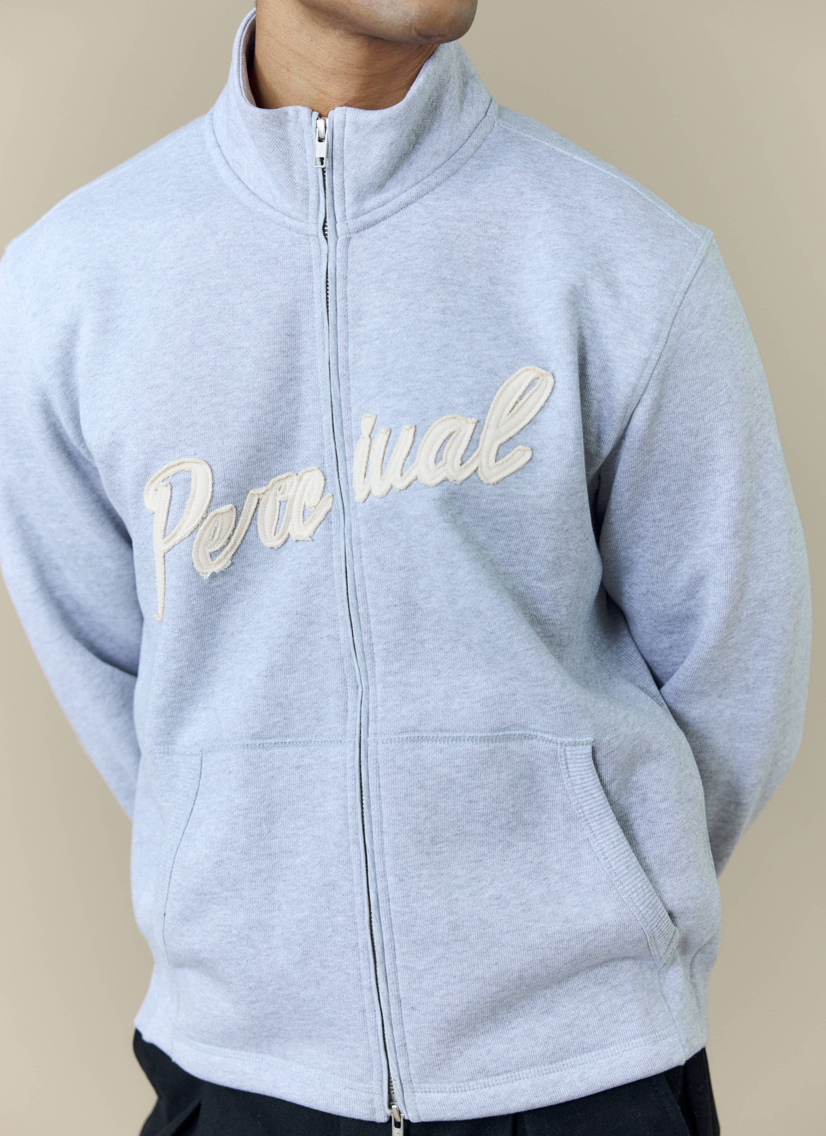 A model wearing the Percival Curtis Boxy Zip Funnel Neck Sweatshirt in athletic grey, showing the cream logo embroidery.