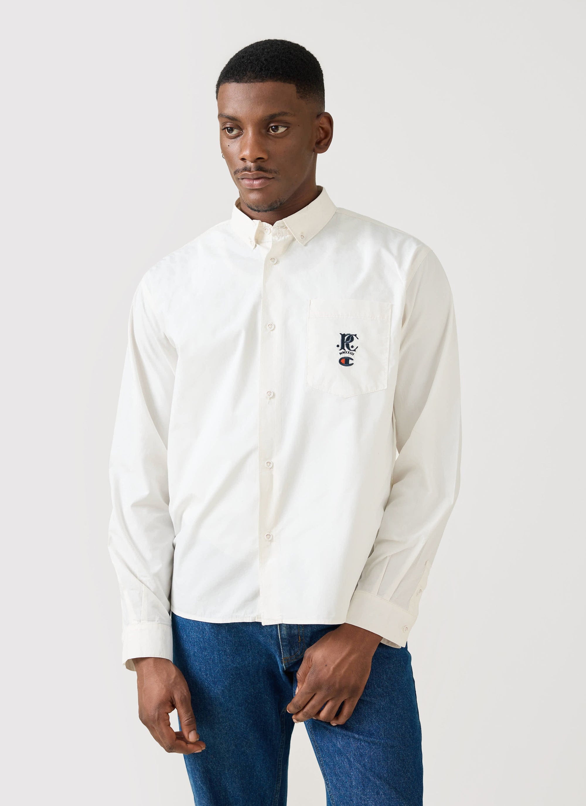 A model wears the Champion x Percival Relaxed Oxford Shirt in ecru against a plain studio background.