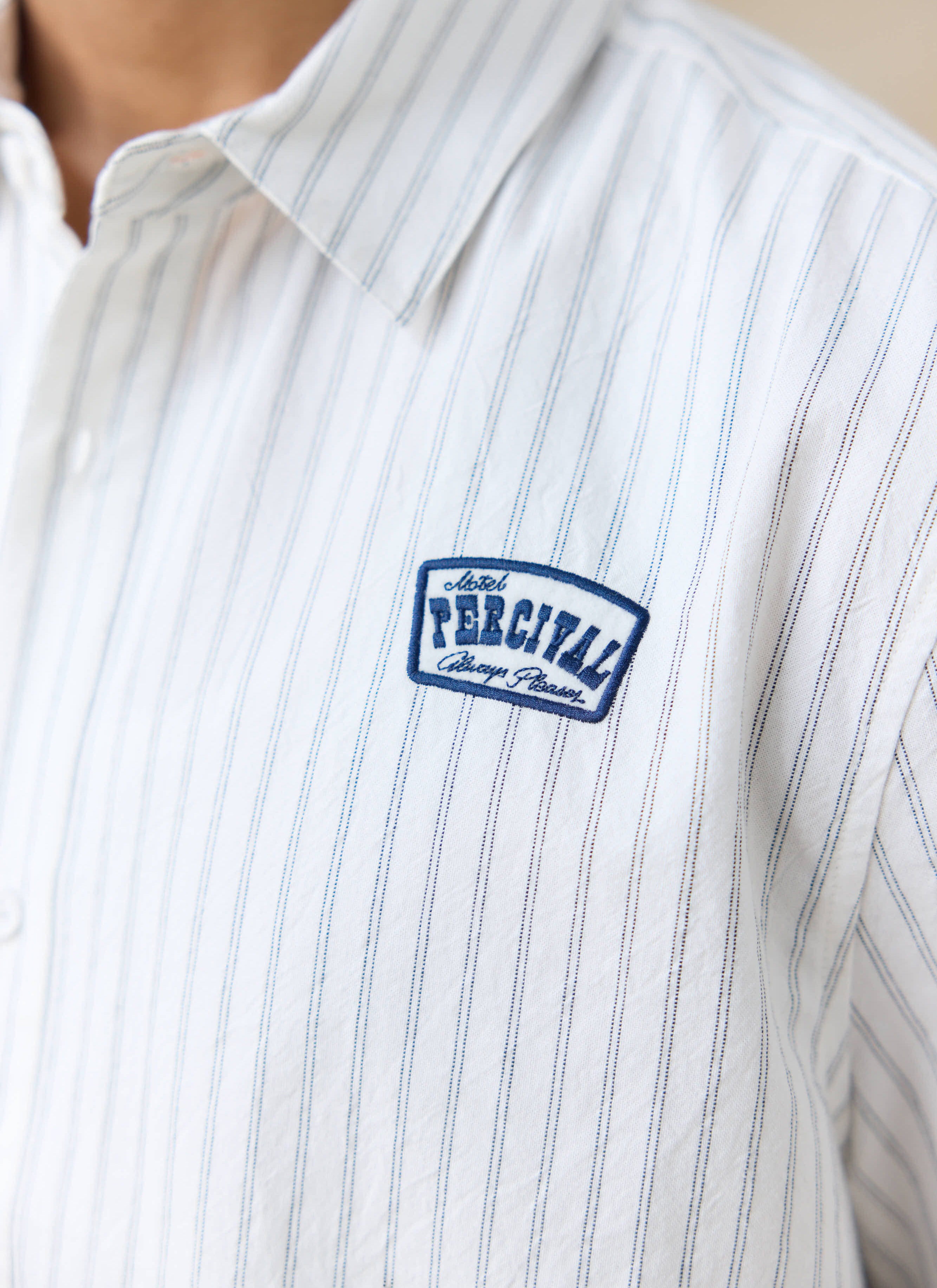 Close-up of the blue embroidered motel badge on the Percival Lucia cream stripe shirt in breathable cotton.