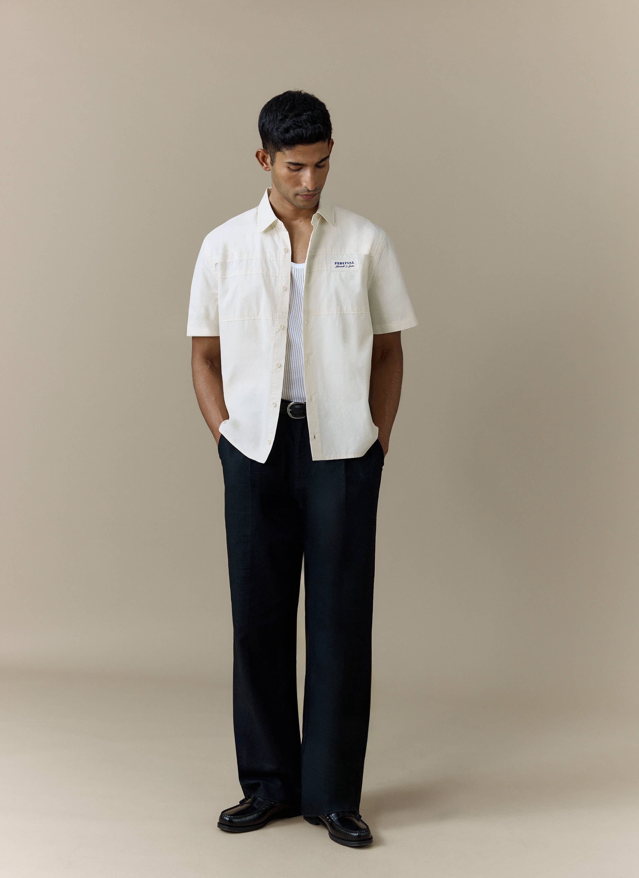 A model wears the Percival Harlow Boxy Shirt in ecru, styled open over a vest with black wide-leg trousers.