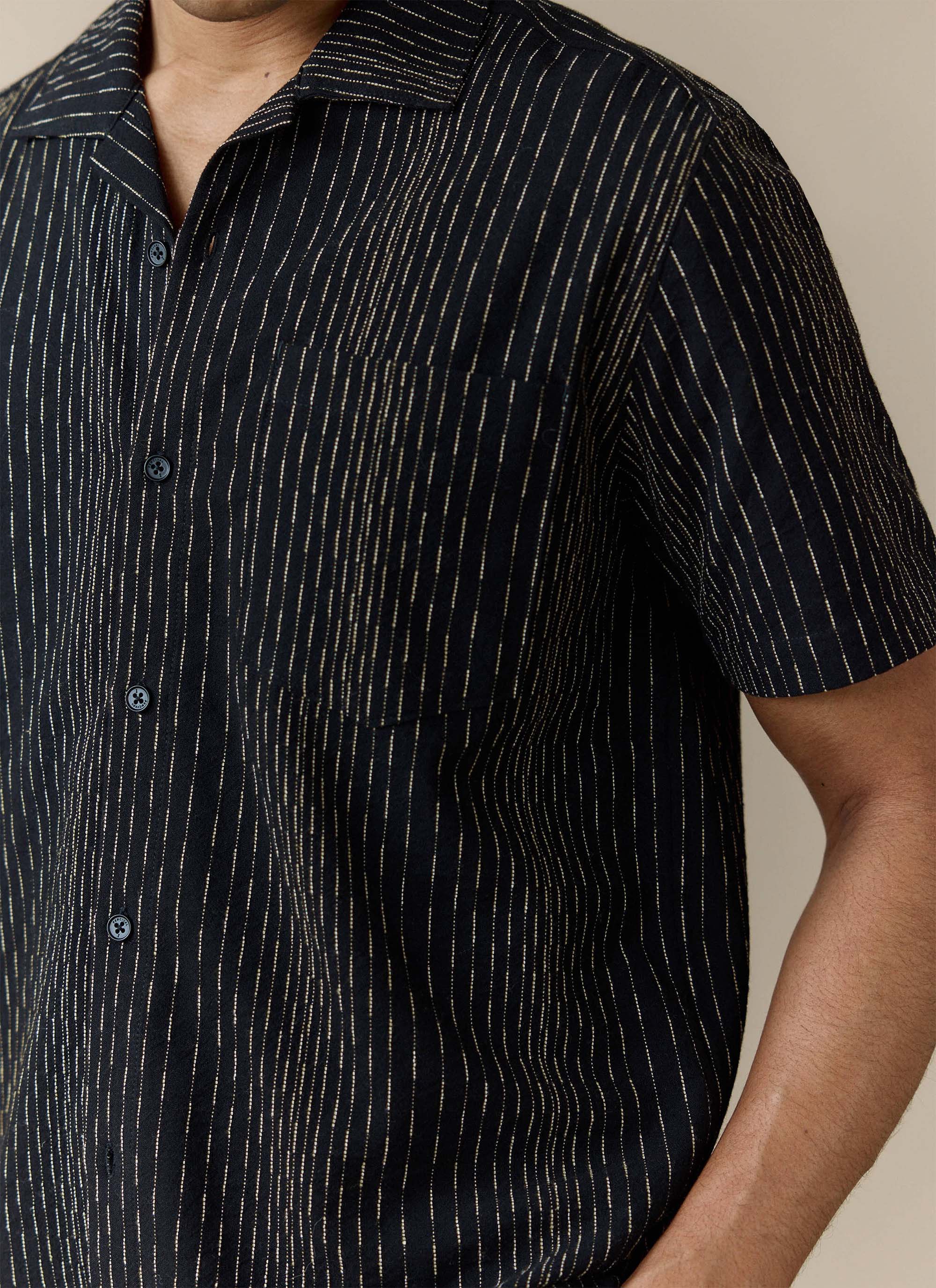 Close-up of a model wearing the black Leland Cuban Shirt from Percival, showing the cotton fabric and vertical stripe detail.