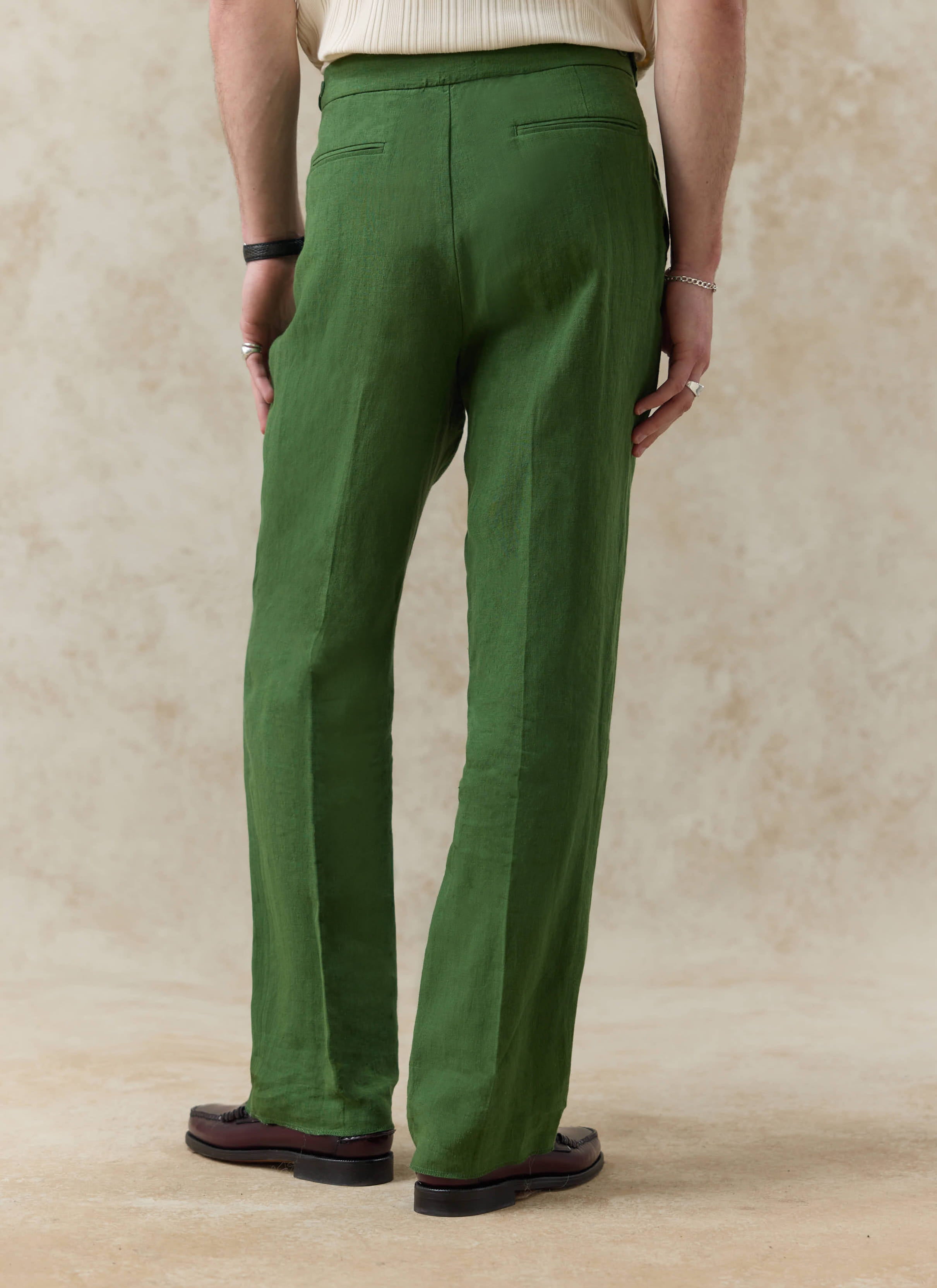 Rear view of the forest green linen pleated tailored trousers by Percival, showing the welt pockets and relaxed fit.