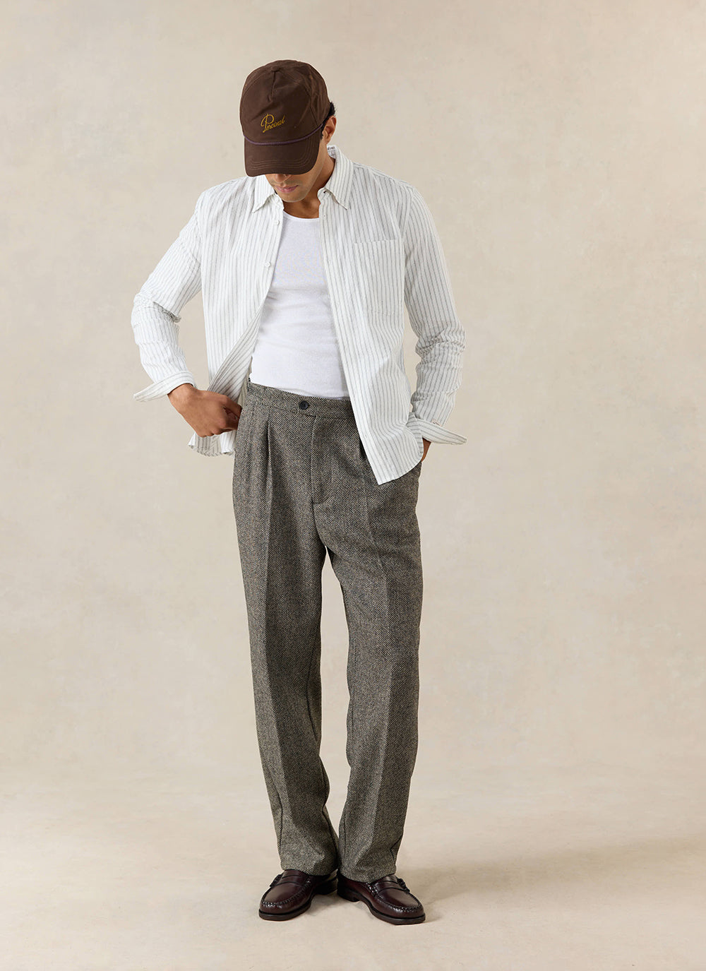A model wears the Percival Fabian Striped Shirt in white cotton, styled with brown pleated trousers and a cap.
