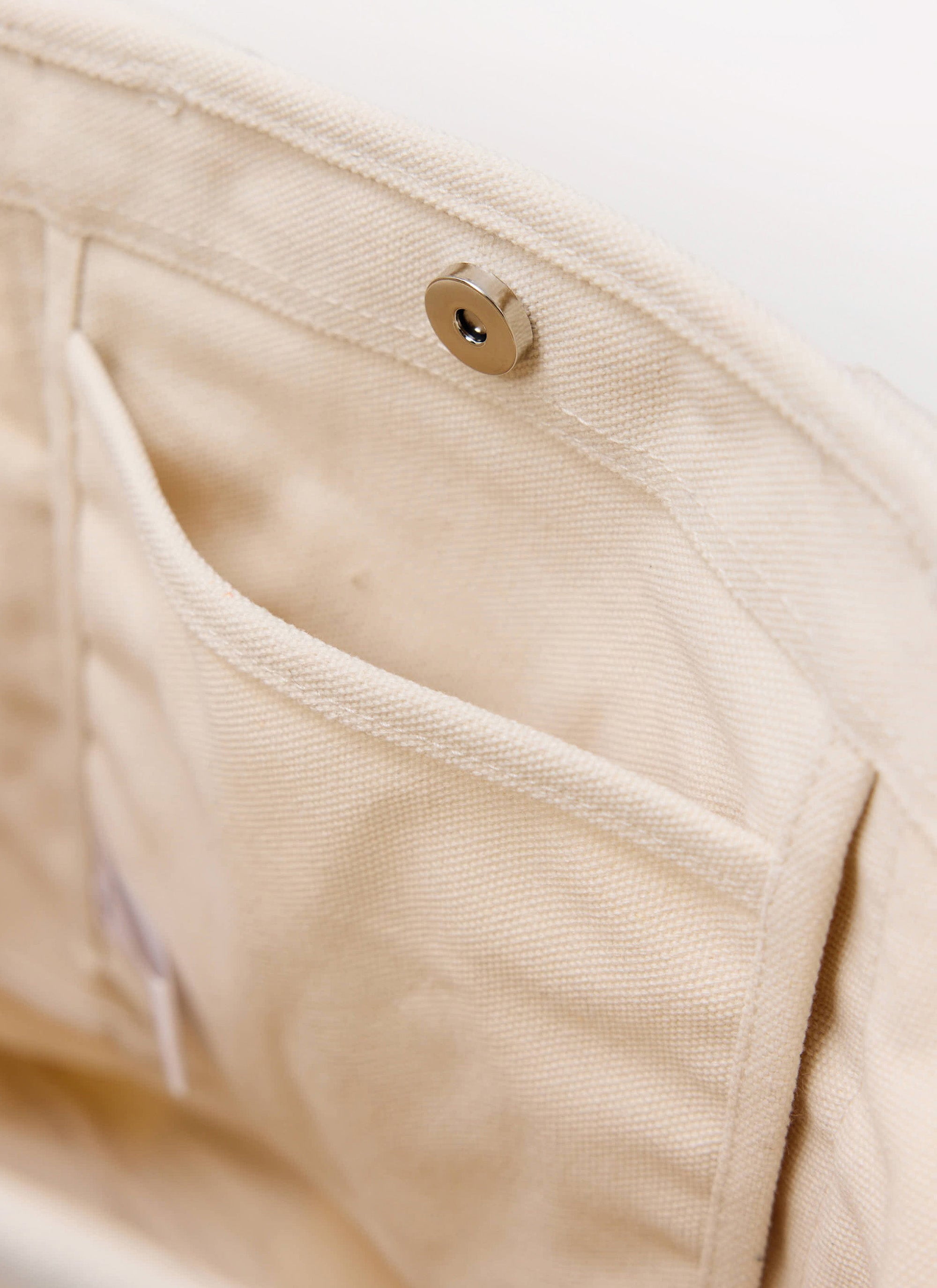 A close-up of the Percival ecru canvas tote bag, detailing the internal pocket and silver magnetic snap closure.