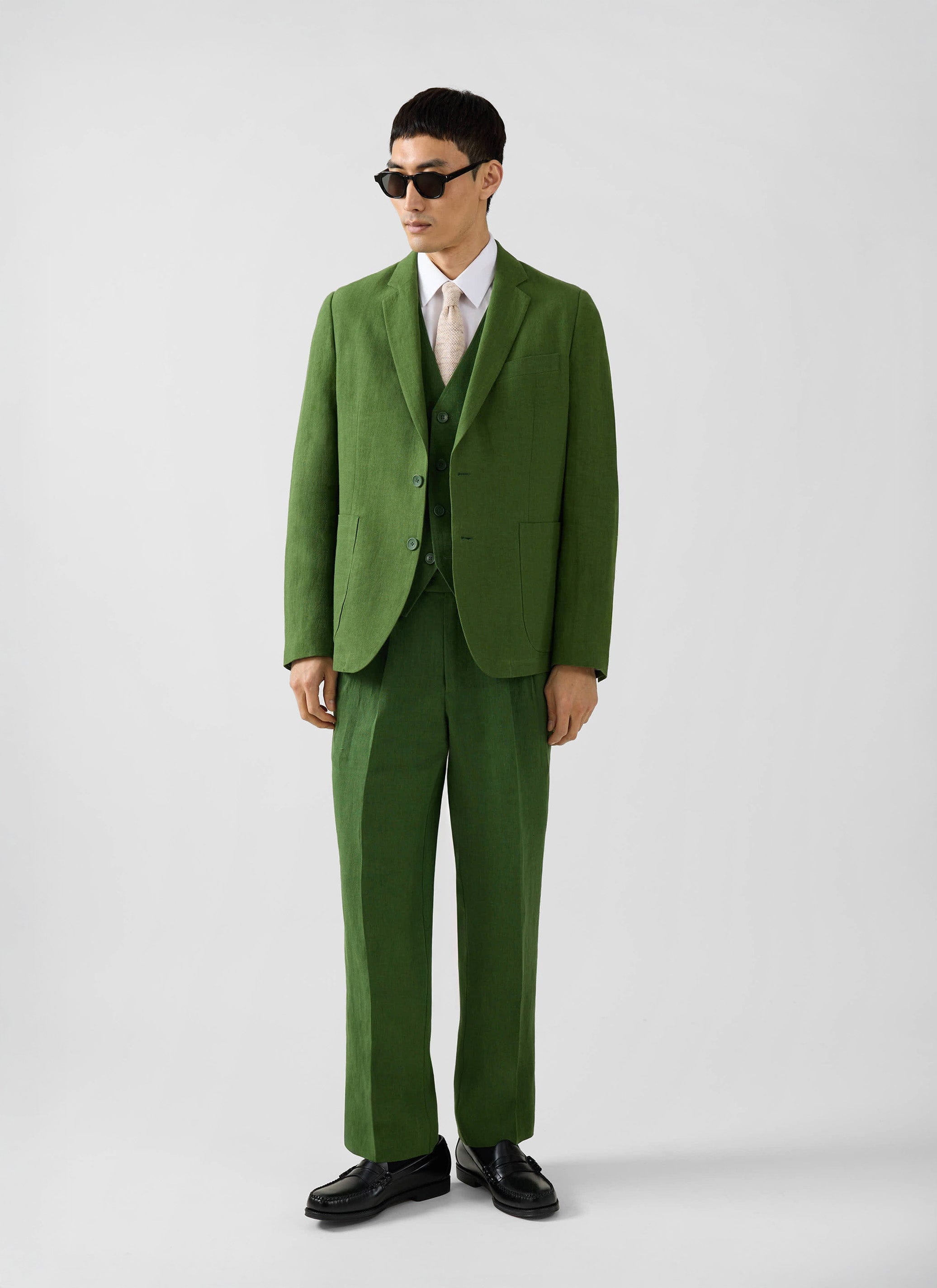 A model wears the full Percival three-piece suit in forest green linen, including the waistcoat, against a studio wall.