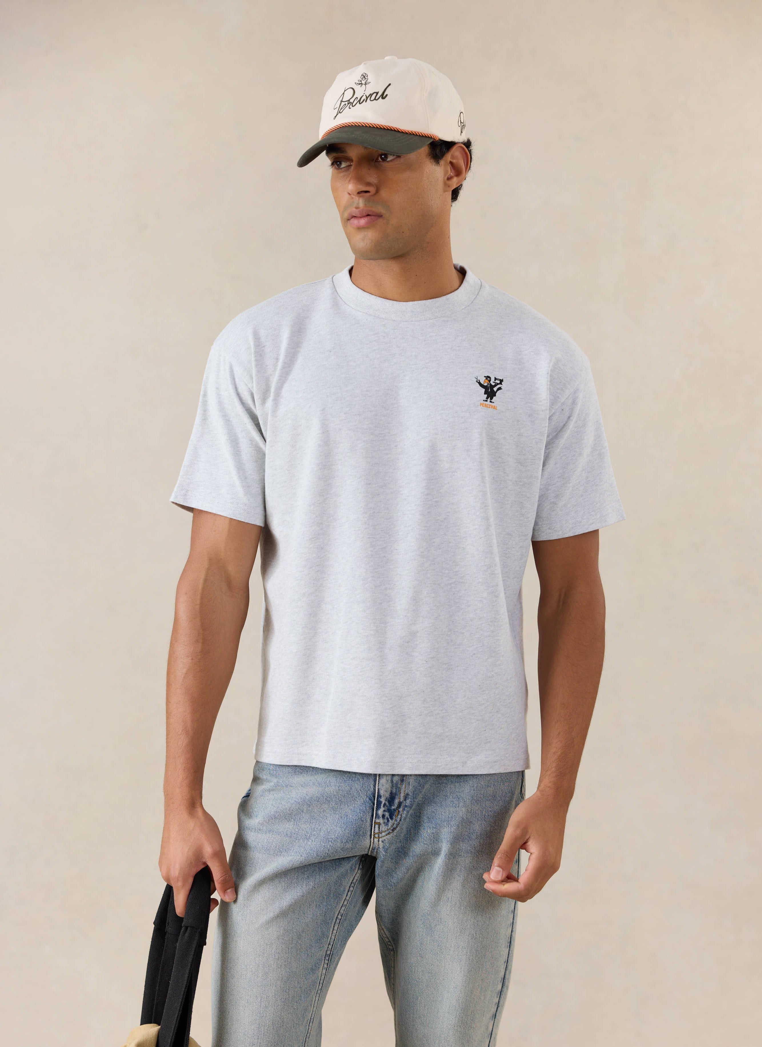 A model wears the Percival Atticus oversized T-shirt in athletic grey organic cotton, styled with light denim and a cap.