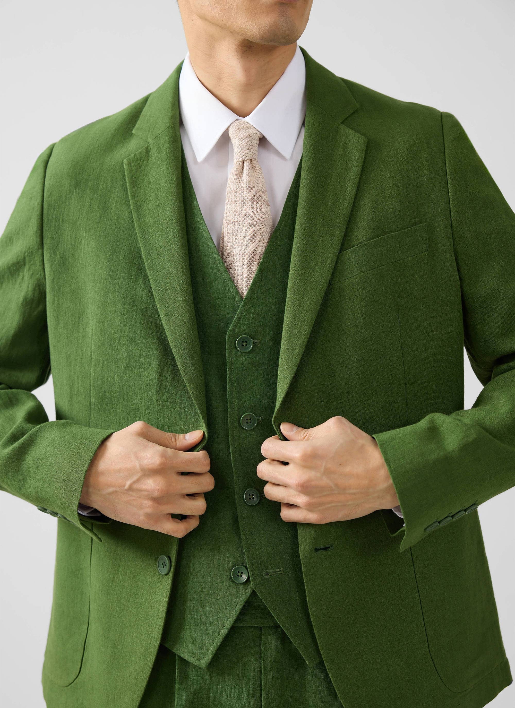 A model wears the complete Percival three-piece suit in forest green linen, with a white shirt and textured beige tie.