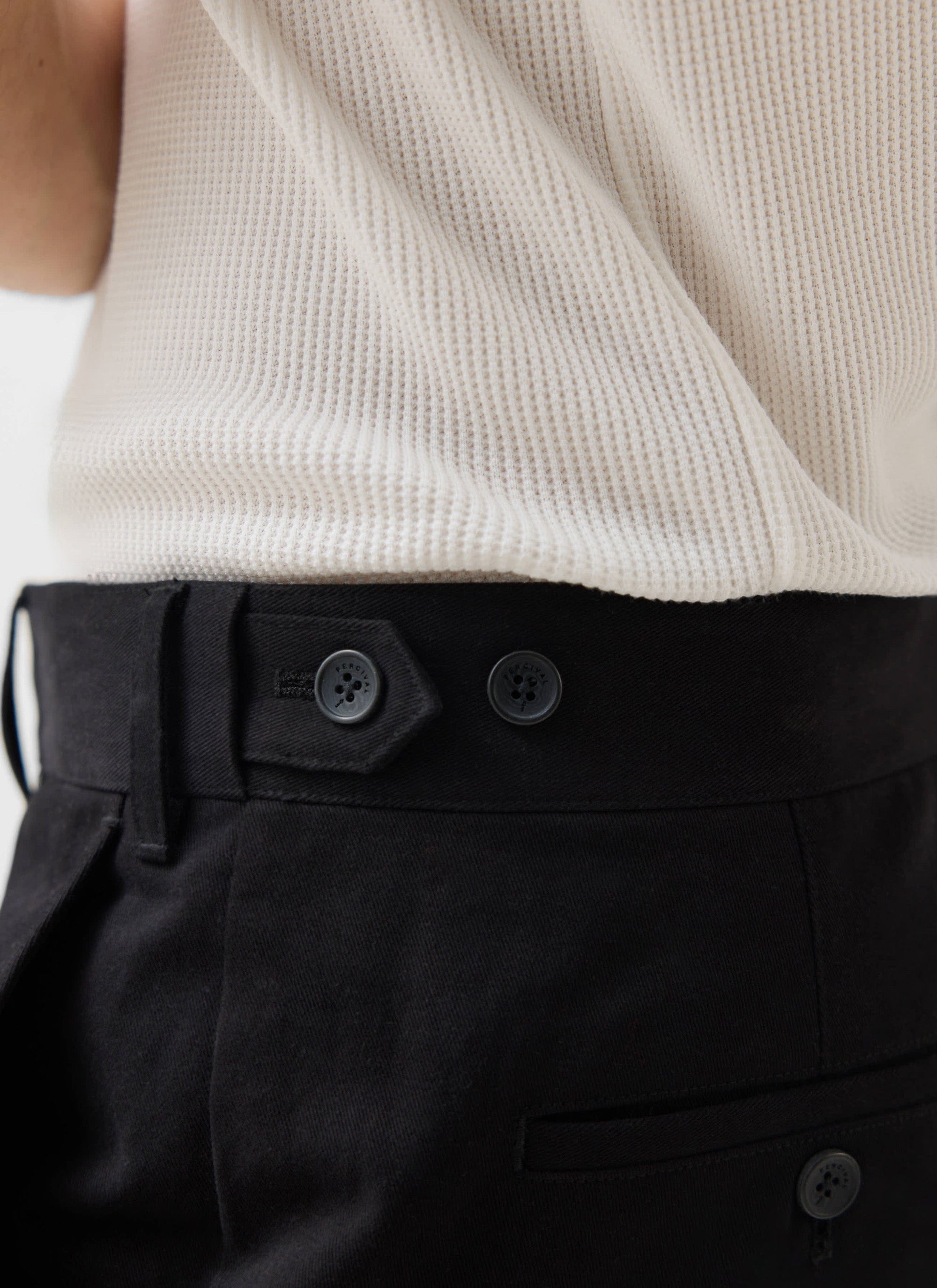 A close-up of a model wearing the Percival Wide Leg Chino in black, showing the cotton twill fabric and button fastening.