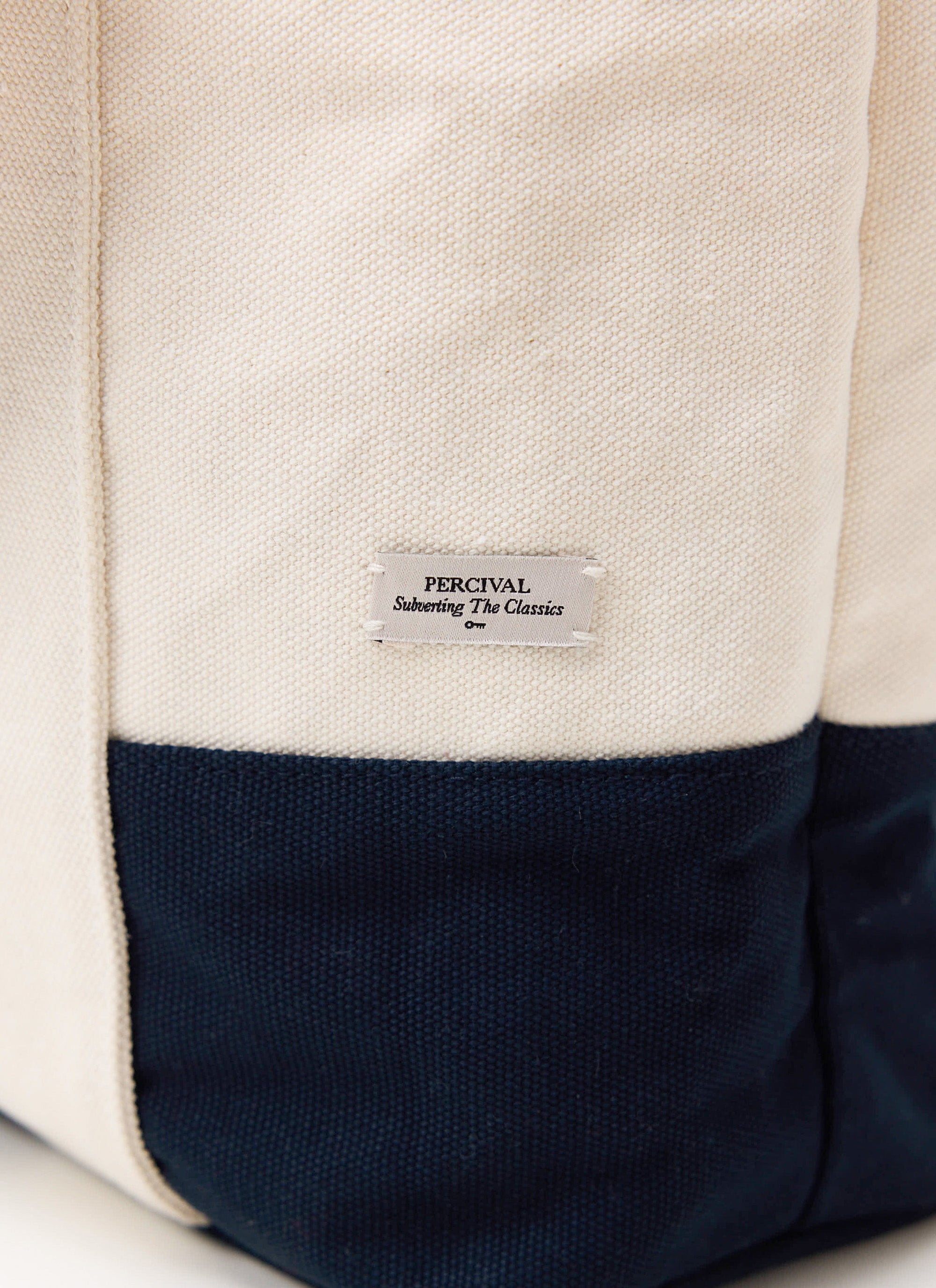 A close-up of the ecru and navy cotton canvas Percival Tote Bag, featuring the 'Subverting The Classics' brand label.