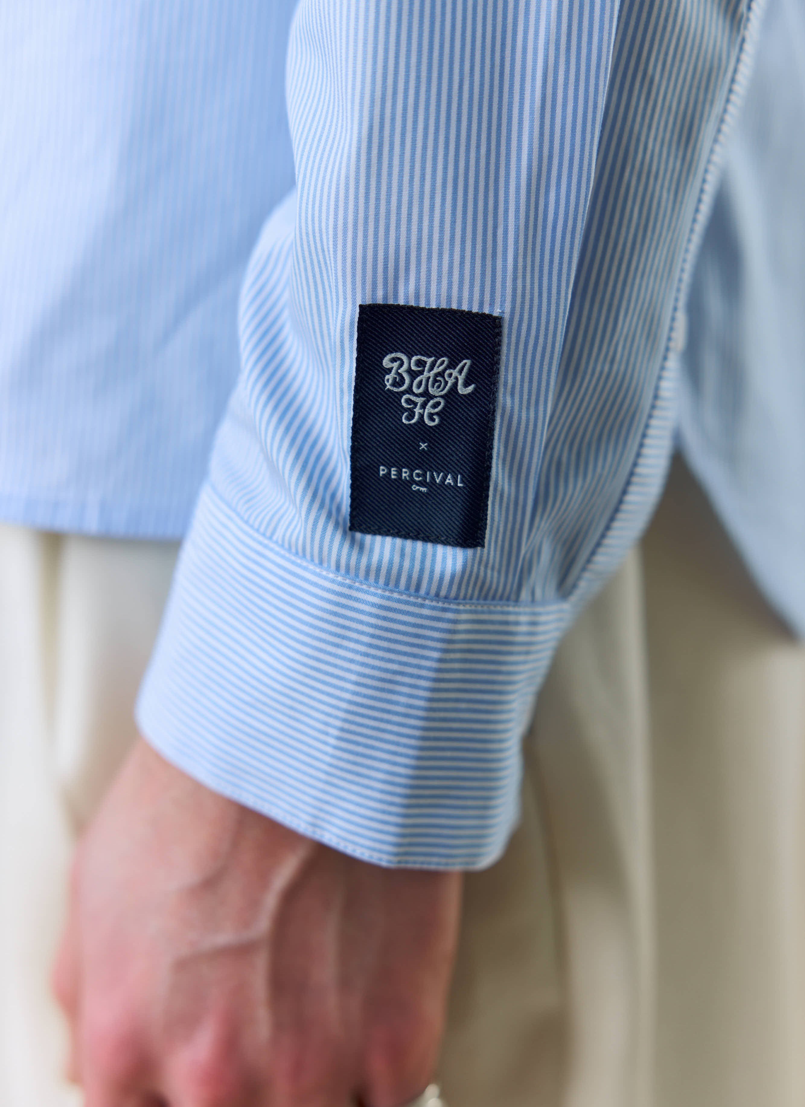 A close-up of the Percival x Brighton & Hove Albion F.C. woven label on the sleeve of the striped Pearce shirt.