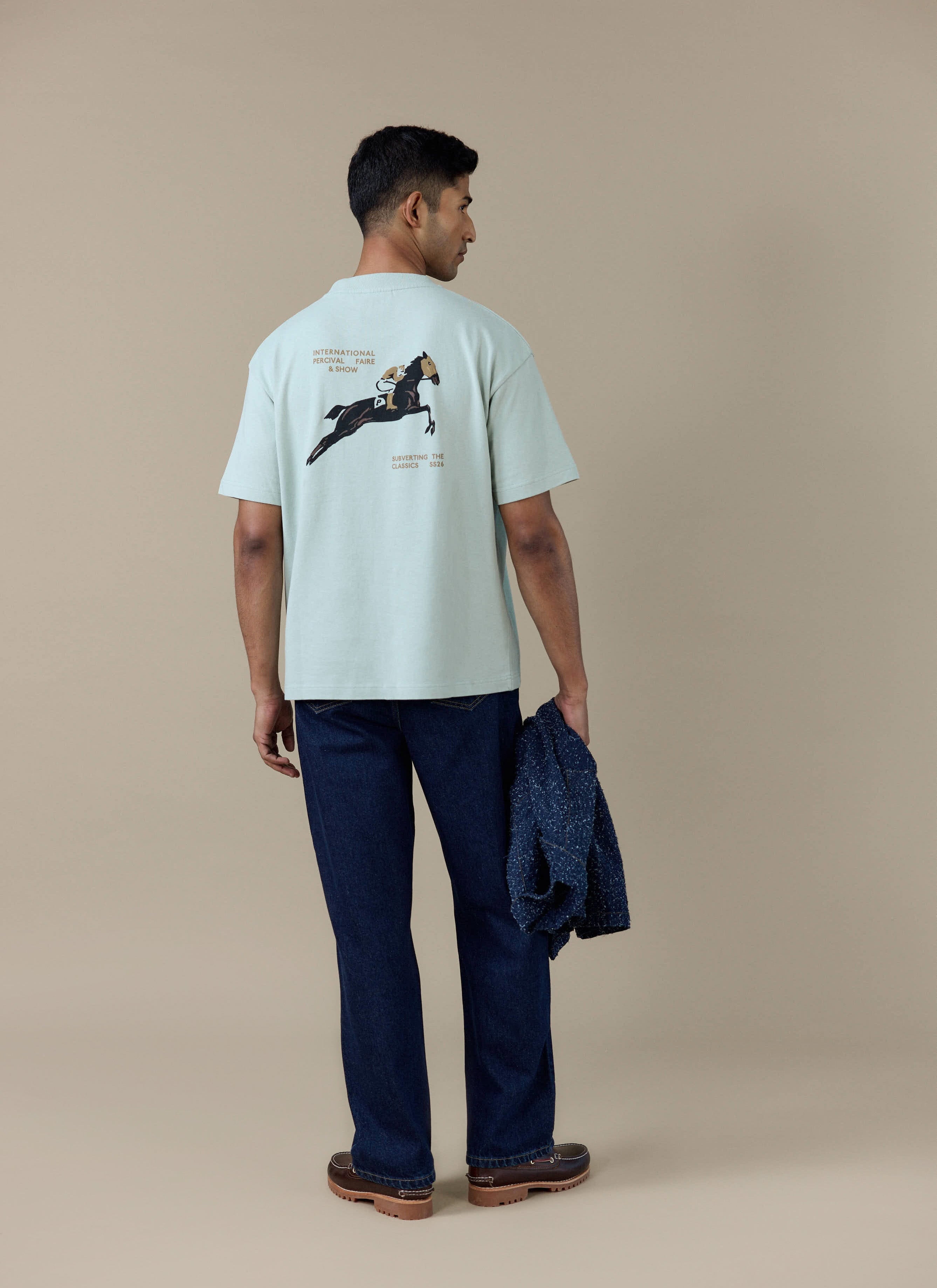Back view of a model wearing the sage Percival Fair and Show Oversized T Shirt, featuring the horse graphic on the back.
