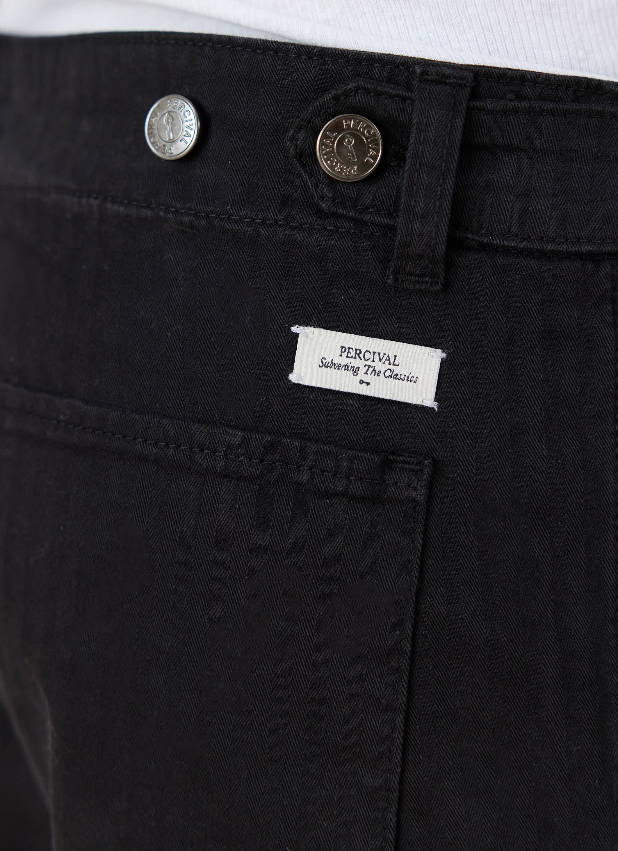 Black cotton Percival Lungo Carpenter Trousers detail showing branded silver buttons and a white woven logo label.