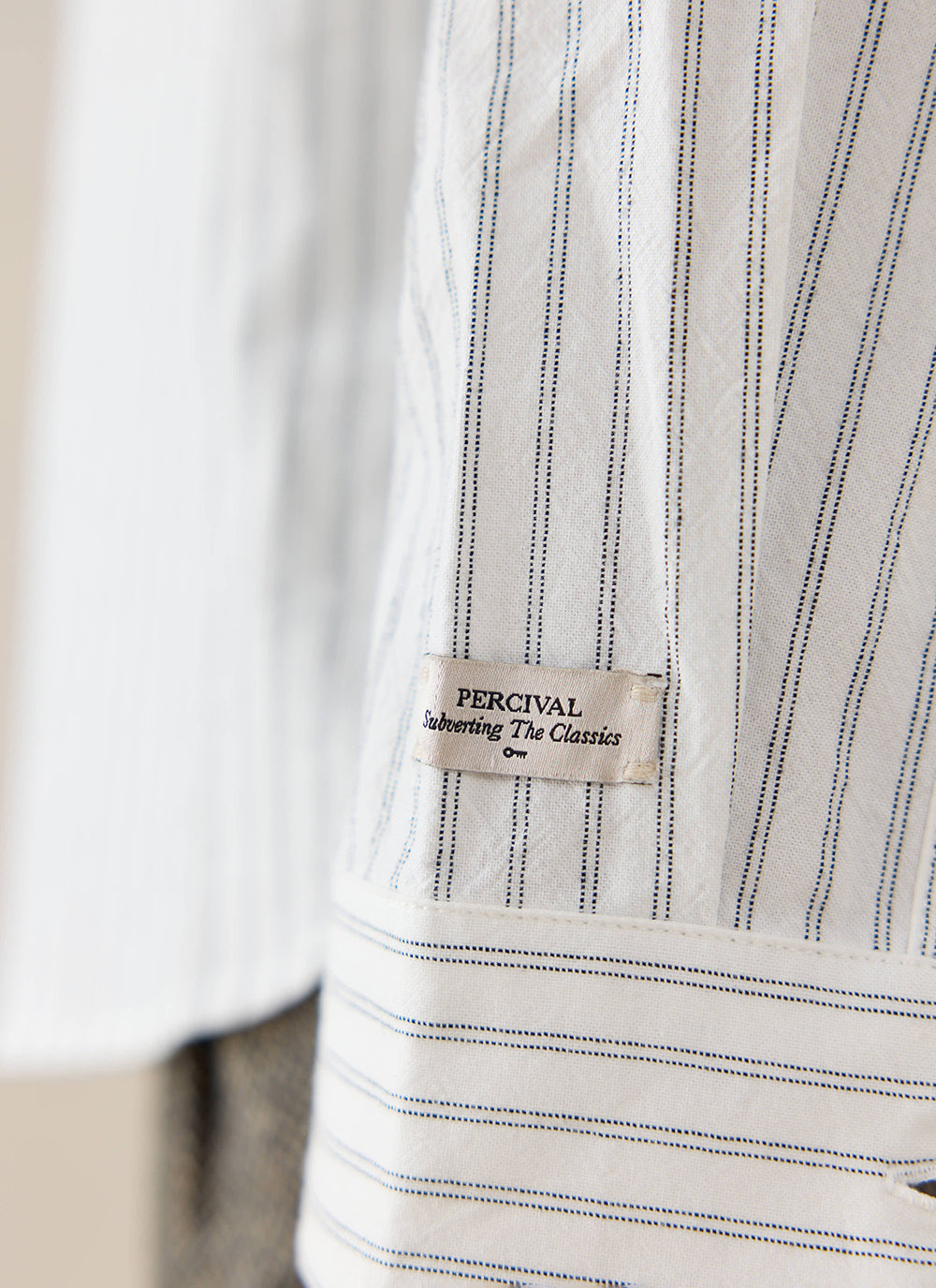 Close-up of the white cotton Fabian Striped Shirt by Percival, featuring the branded label and thin blue vertical stripes.