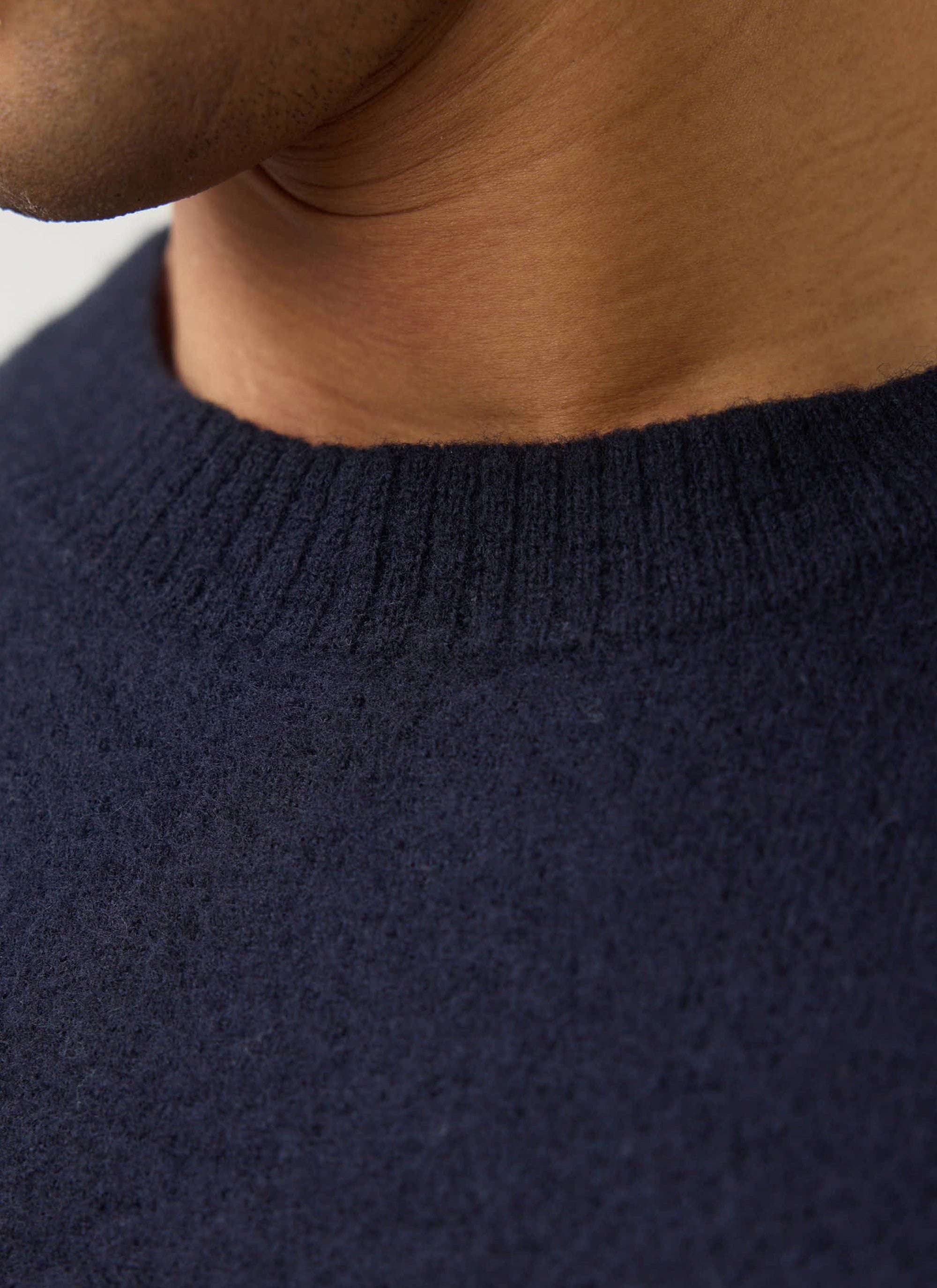 Close up of a model wearing the navy Guinness x Percival merino wool jumper, showing the ribbed neckline detail.