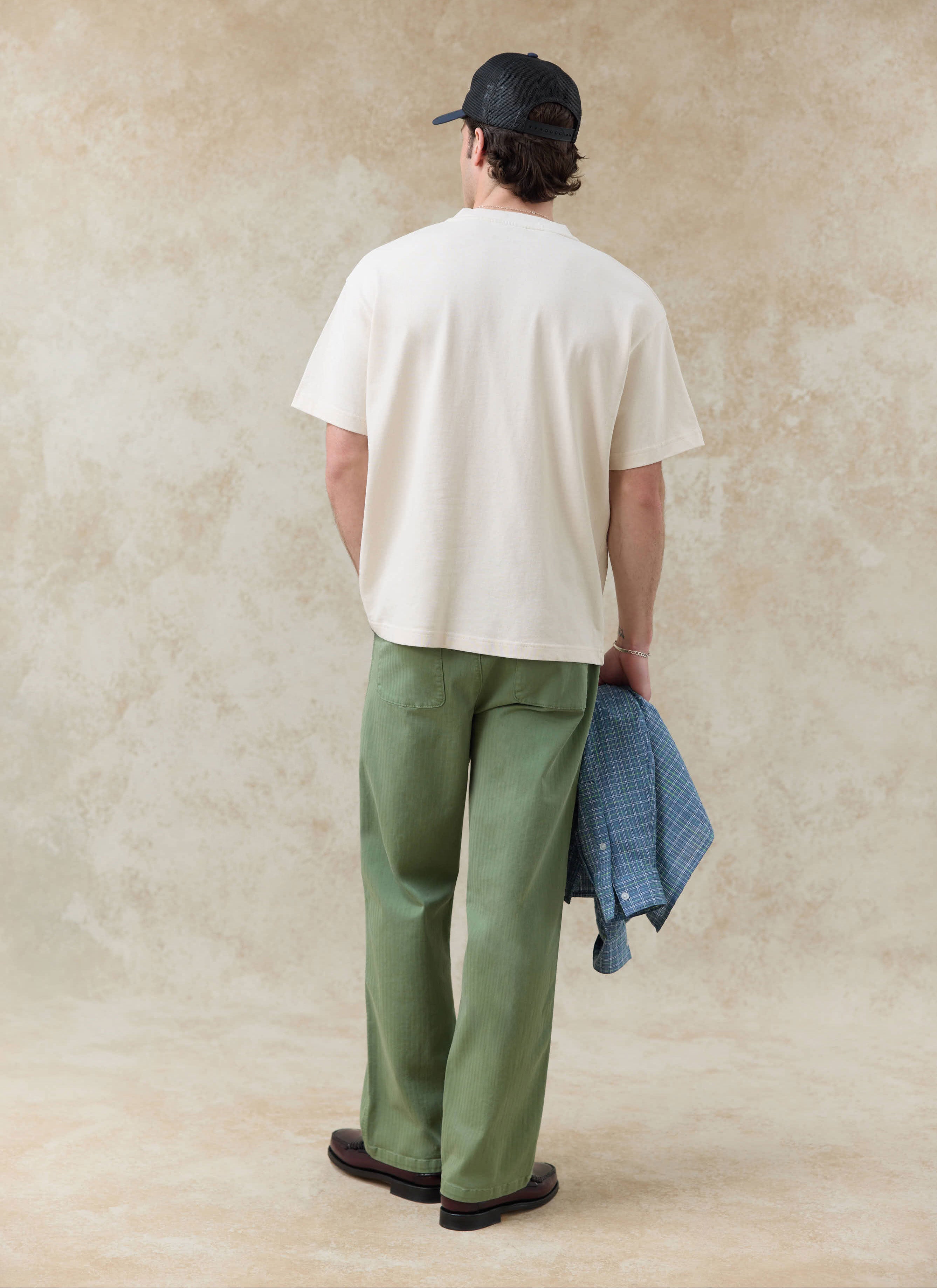 Rear view of the cream Percival Clarke Embroidered T Shirt in organic cotton, styled with green trousers.