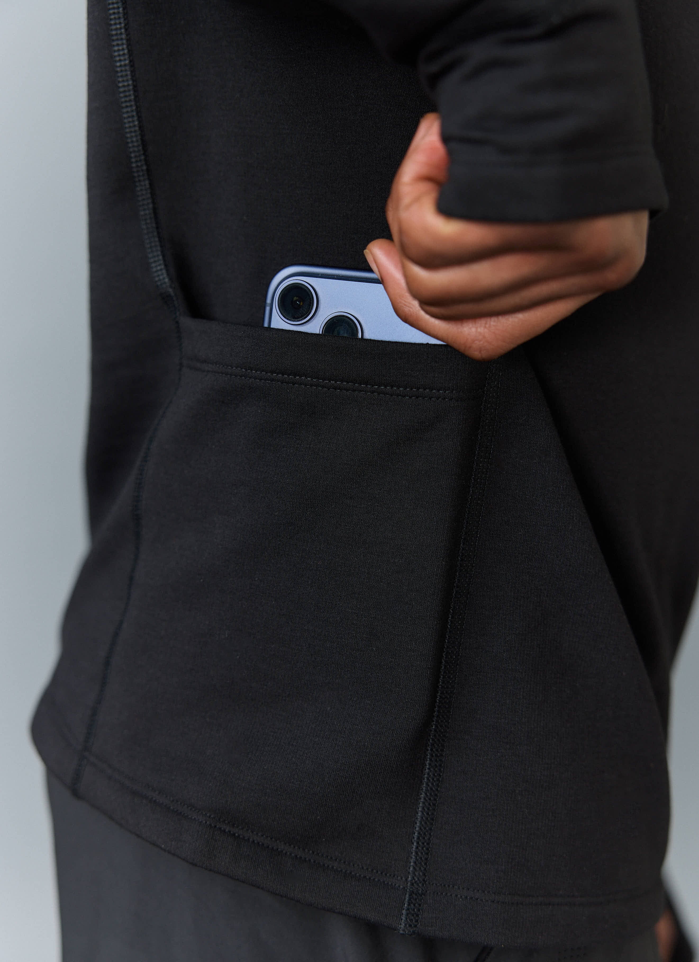 A close-up of the handy low-back stash pocket on the black PCVL Base Layer Quarter Zip Jacket by Percival, holding a phone.