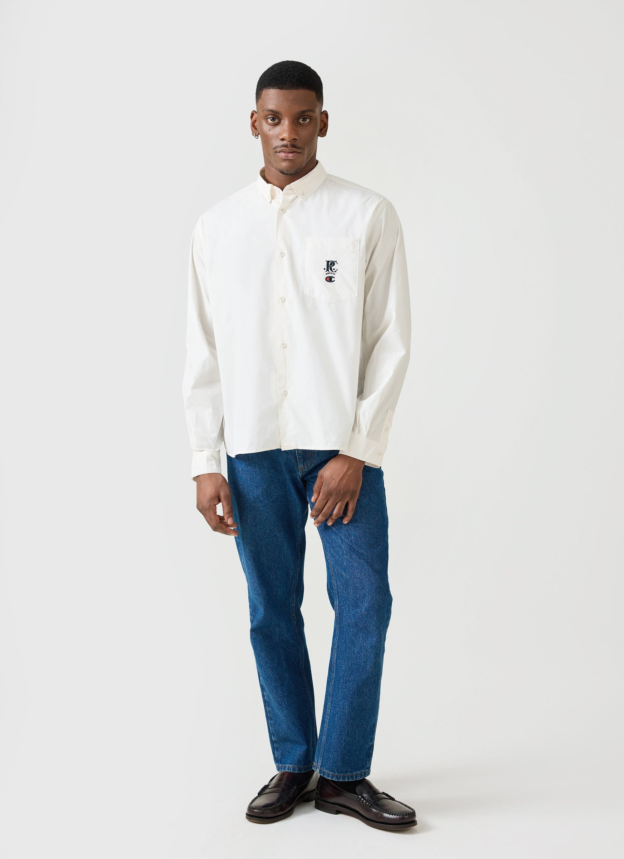 A model wears the ecru Champion x Percival relaxed oxford shirt, styled with blue jeans and loafers.