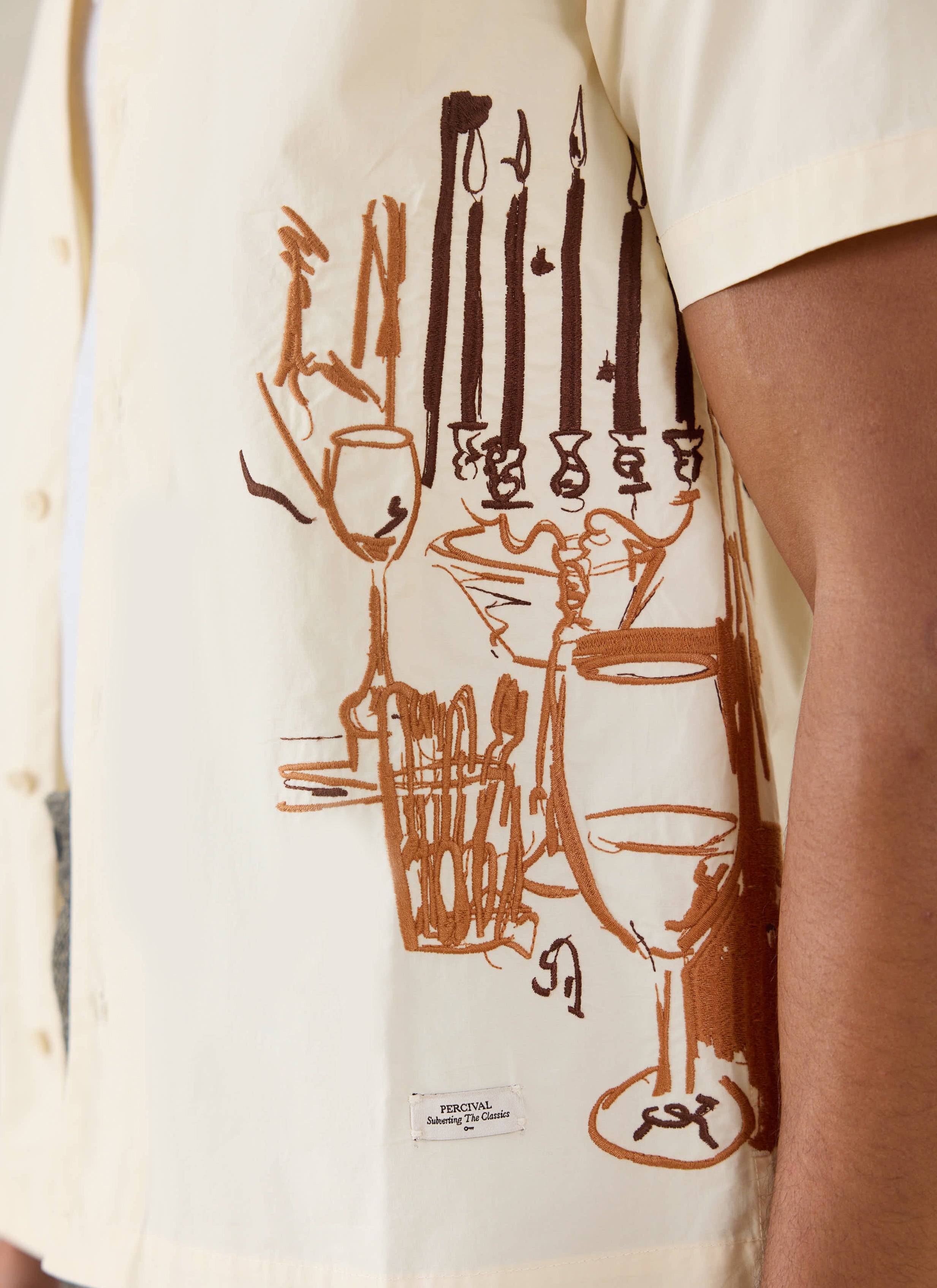 Close-up of the cream cotton Percival Supper Club shirt, showcasing intricate brown dinner party embroidery.