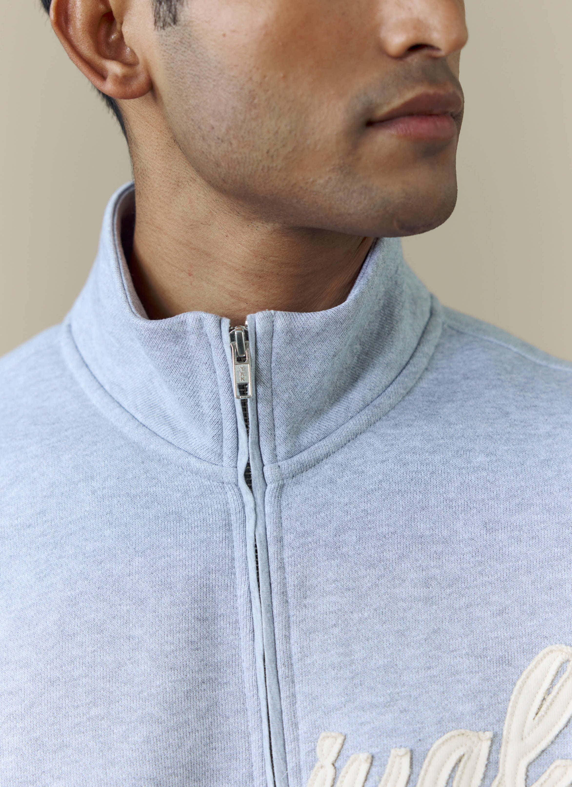 A close-up of a model wearing the Percival Curtis Boxy Zip Funnel Neck Sweatshirt in athletic grey, showing the zip detail.