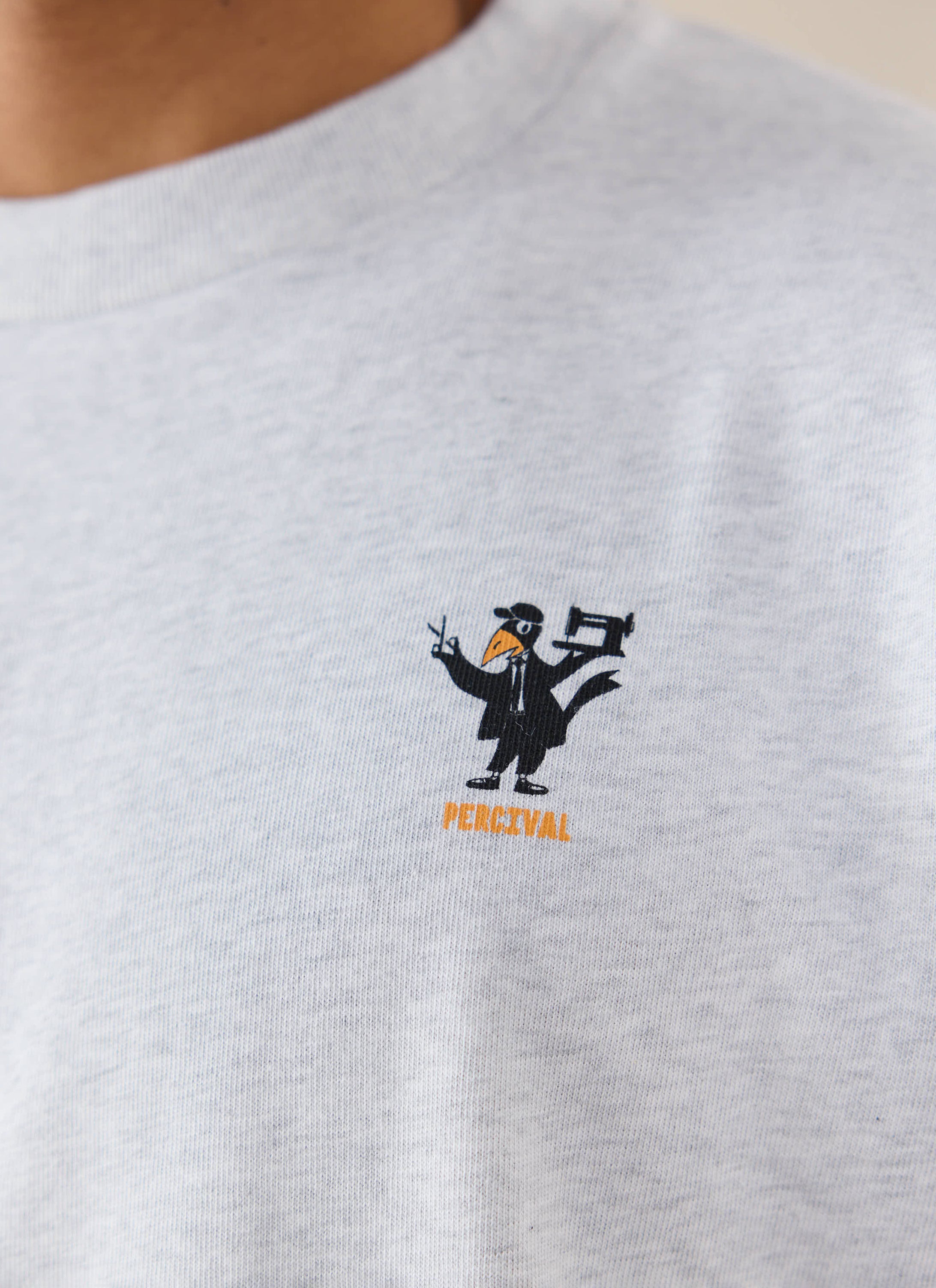 A close-up of a model wearing the athletic grey Percival Atticus T-shirt, showing the detailed chest graphic.