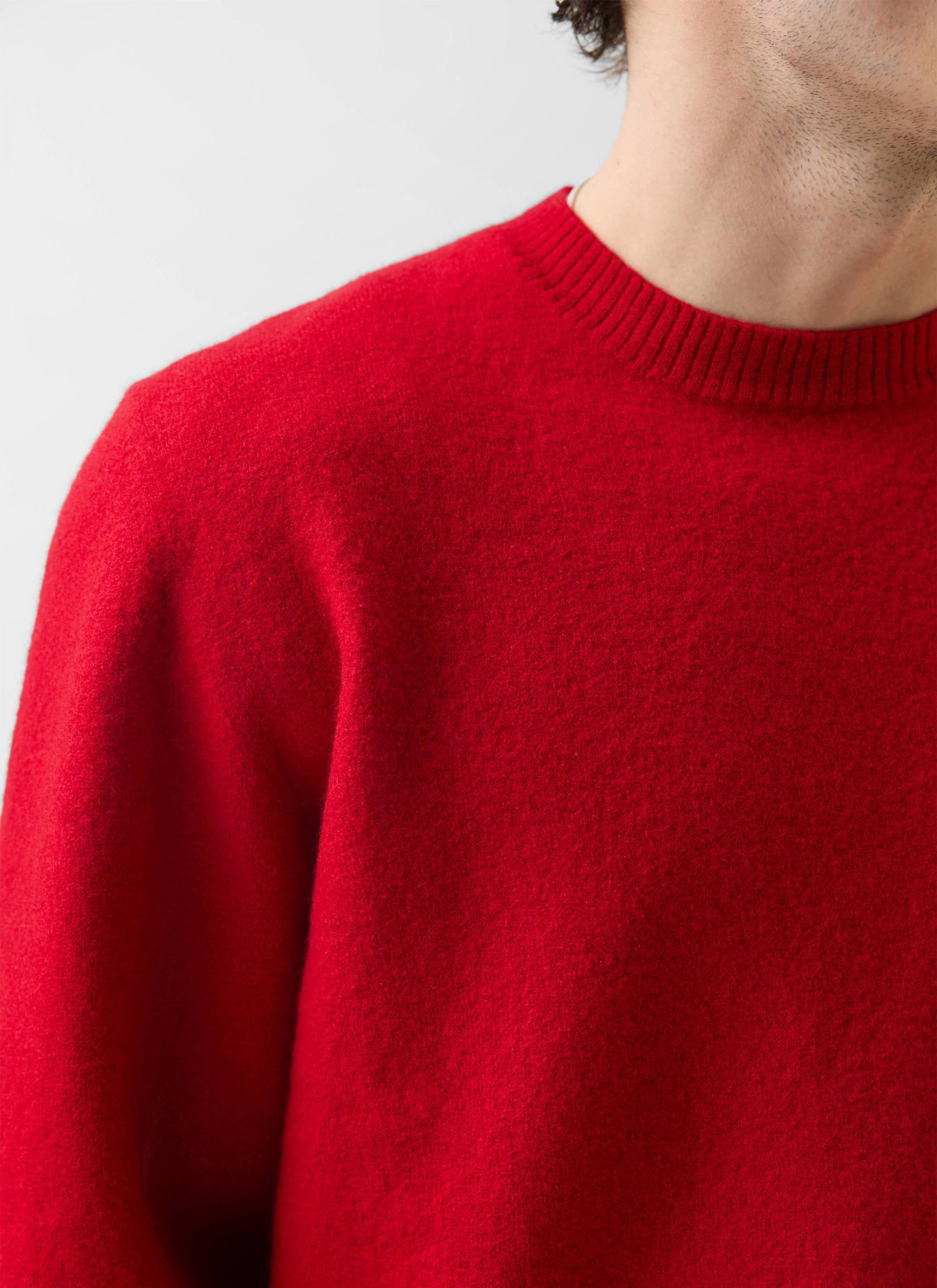 Close up shot of a model wearing the Percival Felted Regular Jumper in red merino wool, showing the shoulder and neckline.