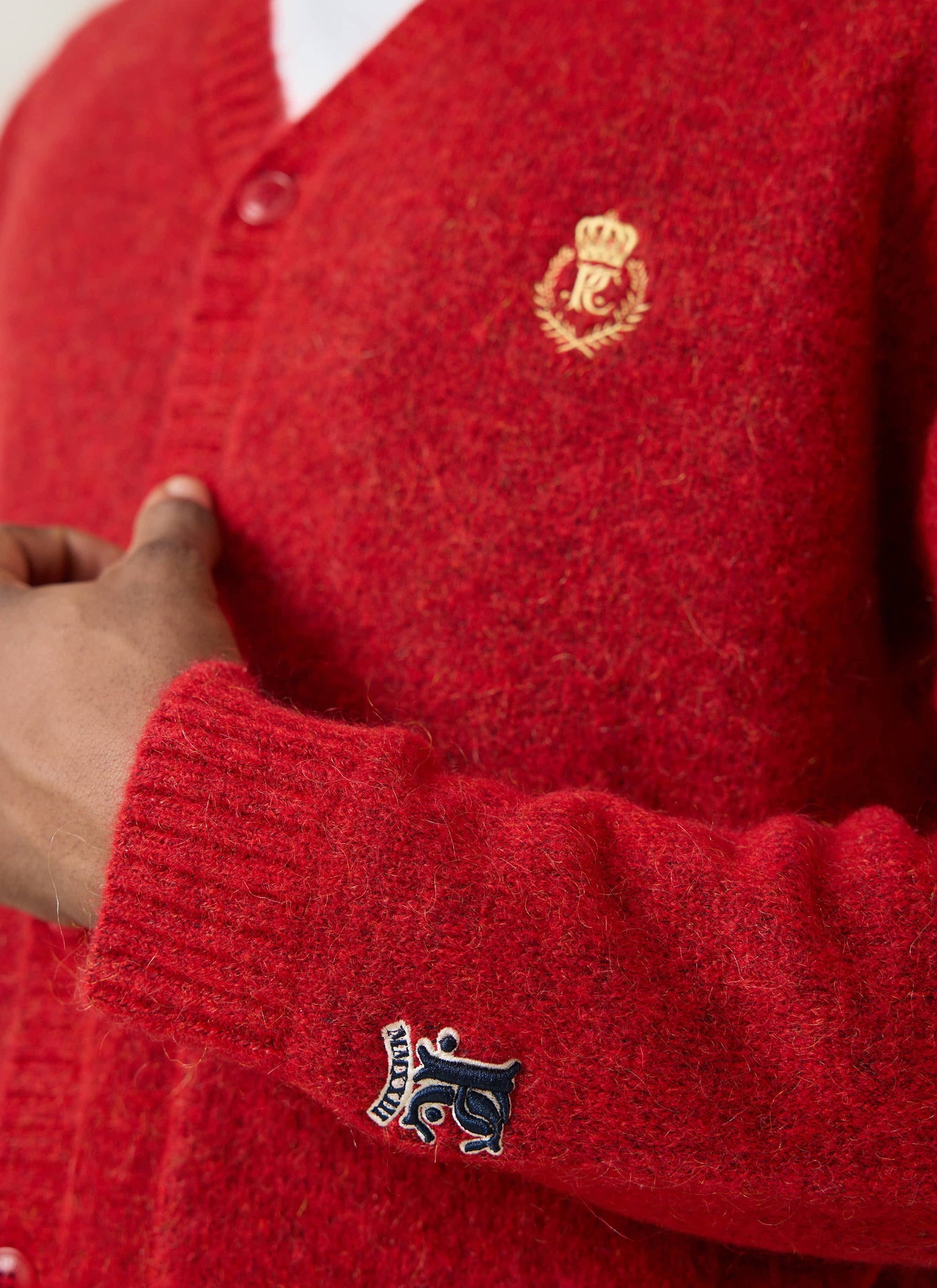 A close-up of the Champion x Percival red mohair cardigan showing the gold chest crest and navy sleeve embroidery.