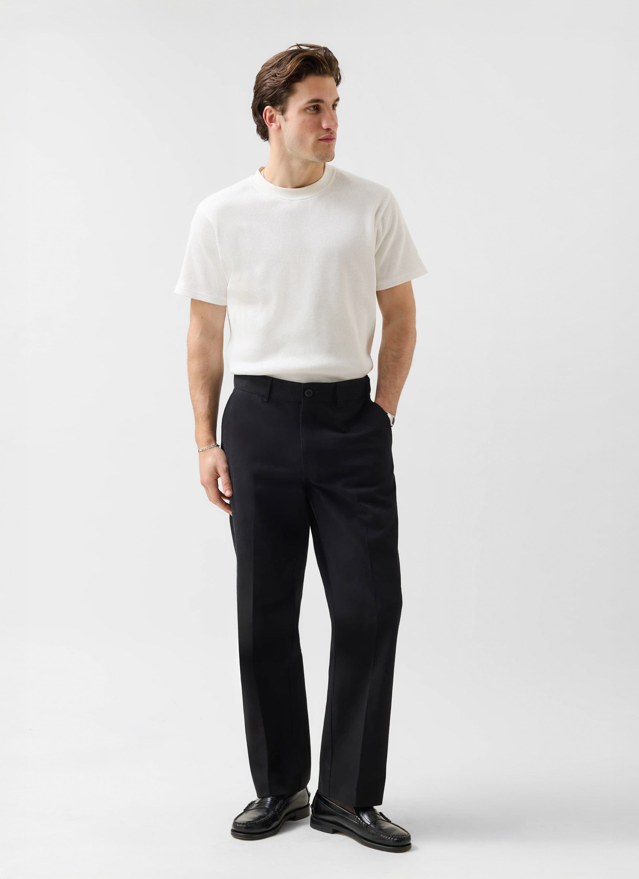 A man models the black Wide Leg Chino from Percival, styled with a white t-shirt and loafers in a studio.