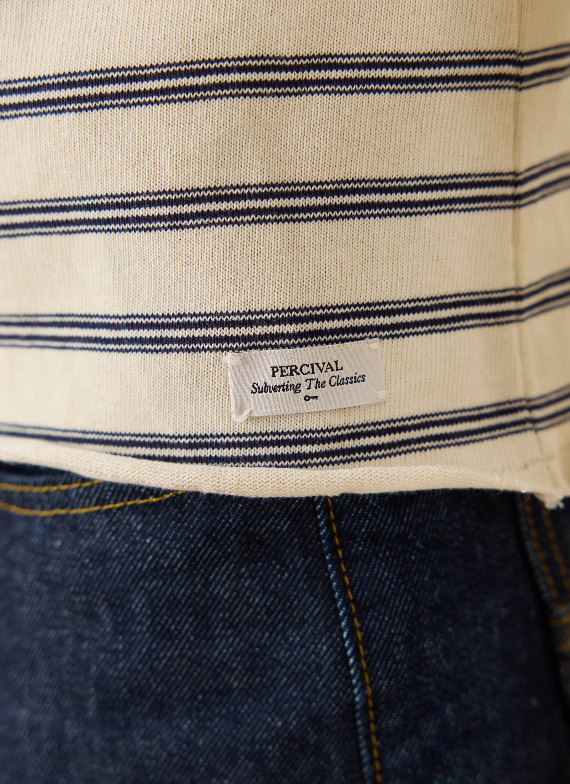 Close-up of the Percival brand tag and raw hem on the white striped organic cotton Arlo long sleeve Breton t-shirt.