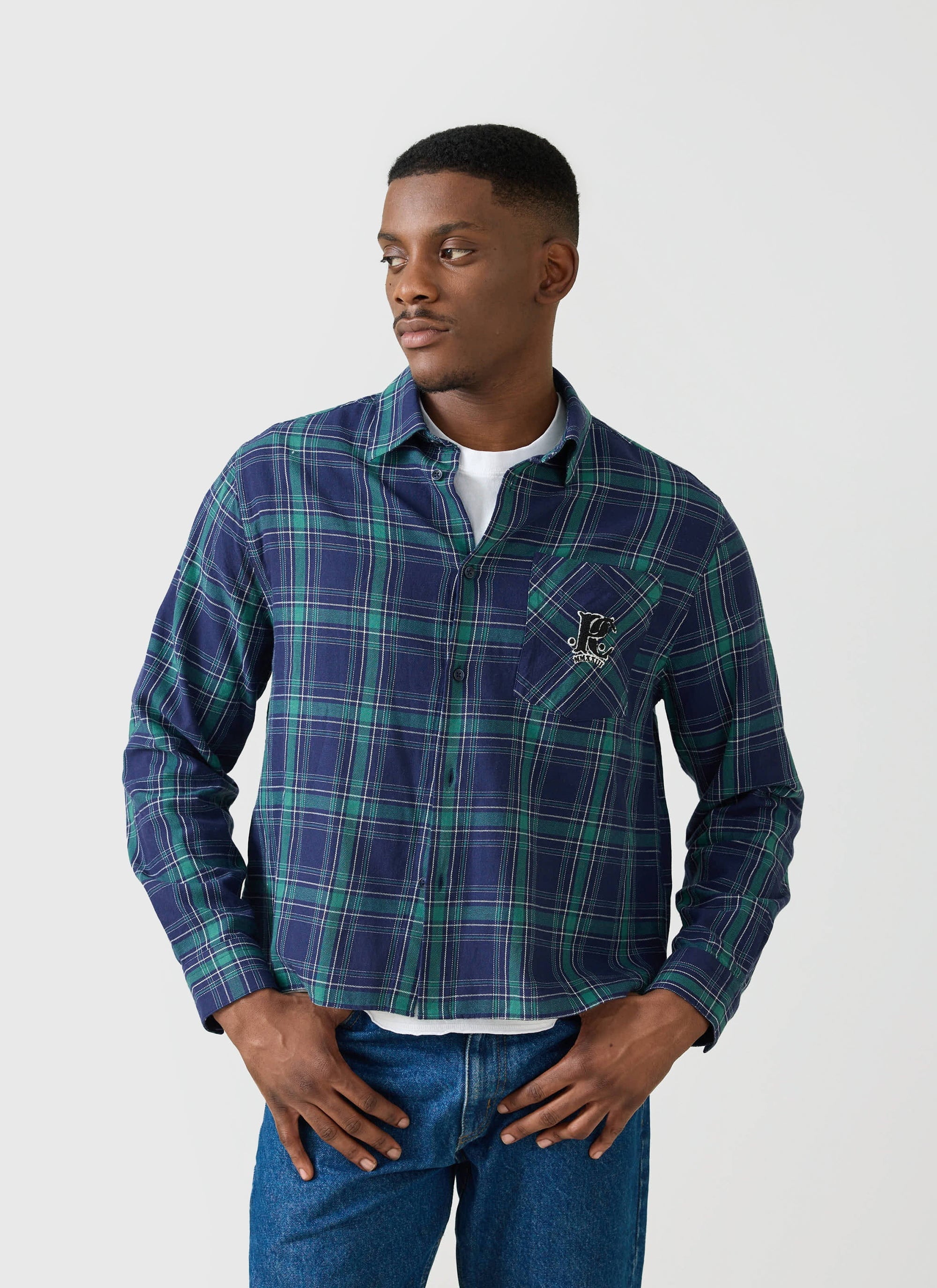 A model wears the Champion x Percival check long sleeve shirt in a blue and green tartan, styled open over a white t-shirt.