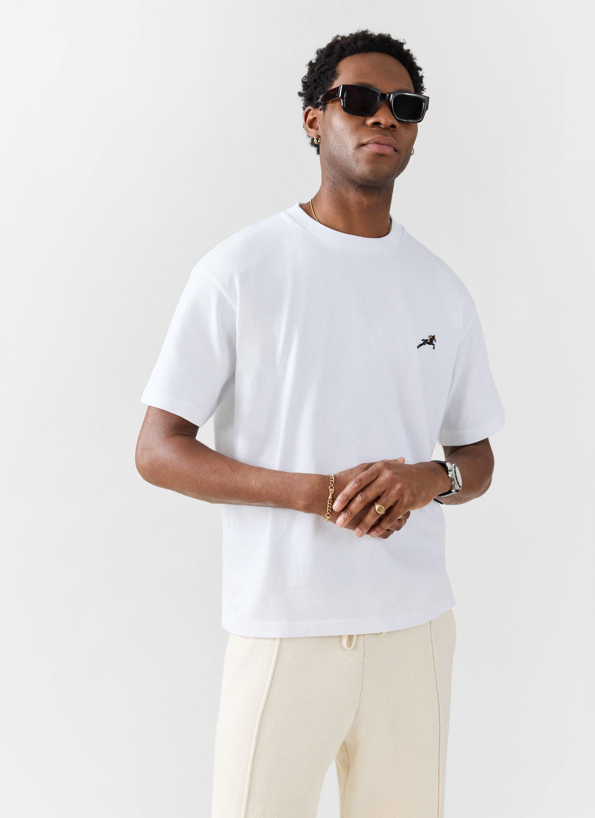 A model wears the Percival Galloping Horse embroidered t-shirt in white, styled with cream trousers and sunglasses.