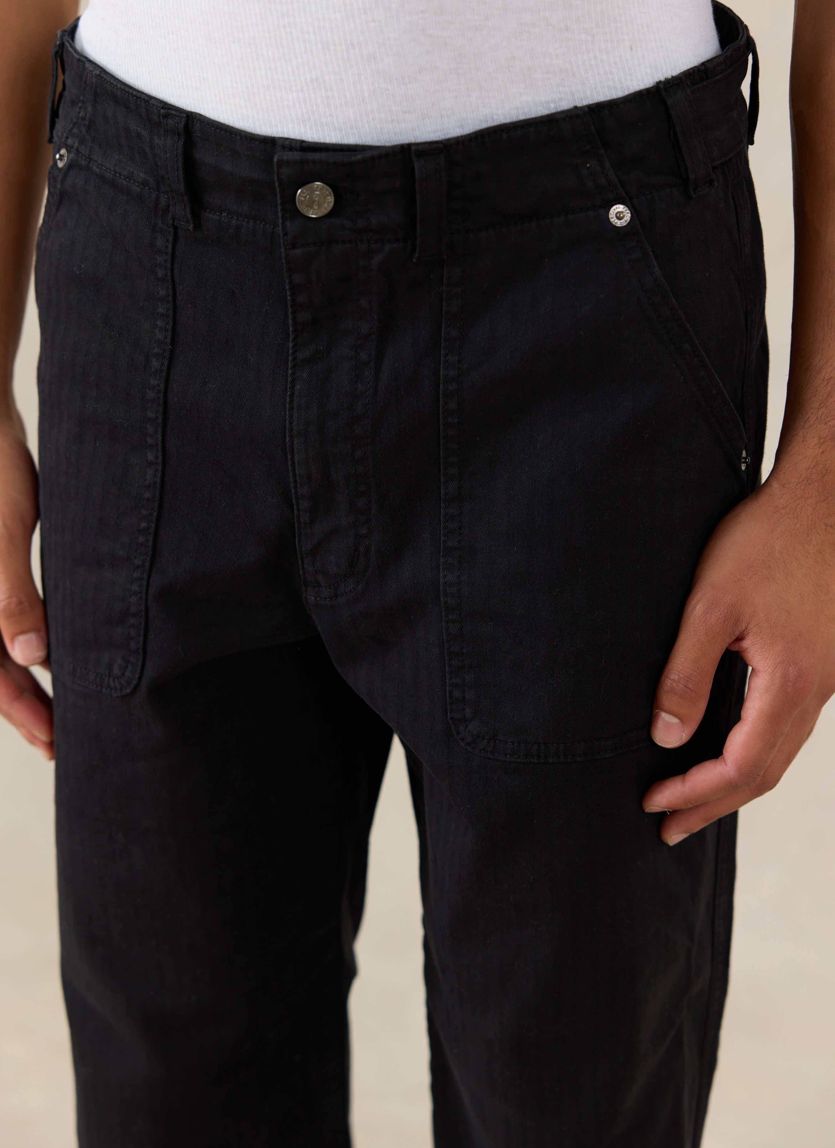 Close-up of a model wearing black Percival Lungo Carpenter Trousers, highlighting the patch pockets and metallic hardware.