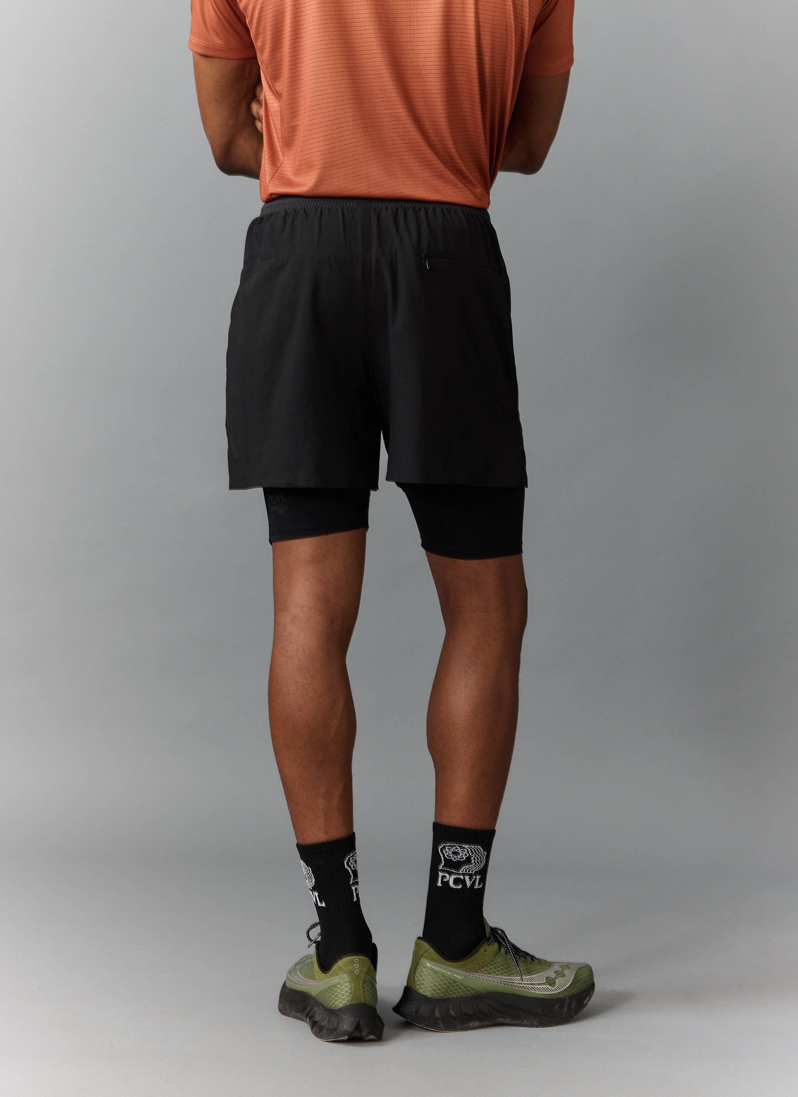 A model wears the black PCVL 2 in 1 Shorts from Percival, seen from behind to show the fit and secure rear pocket.