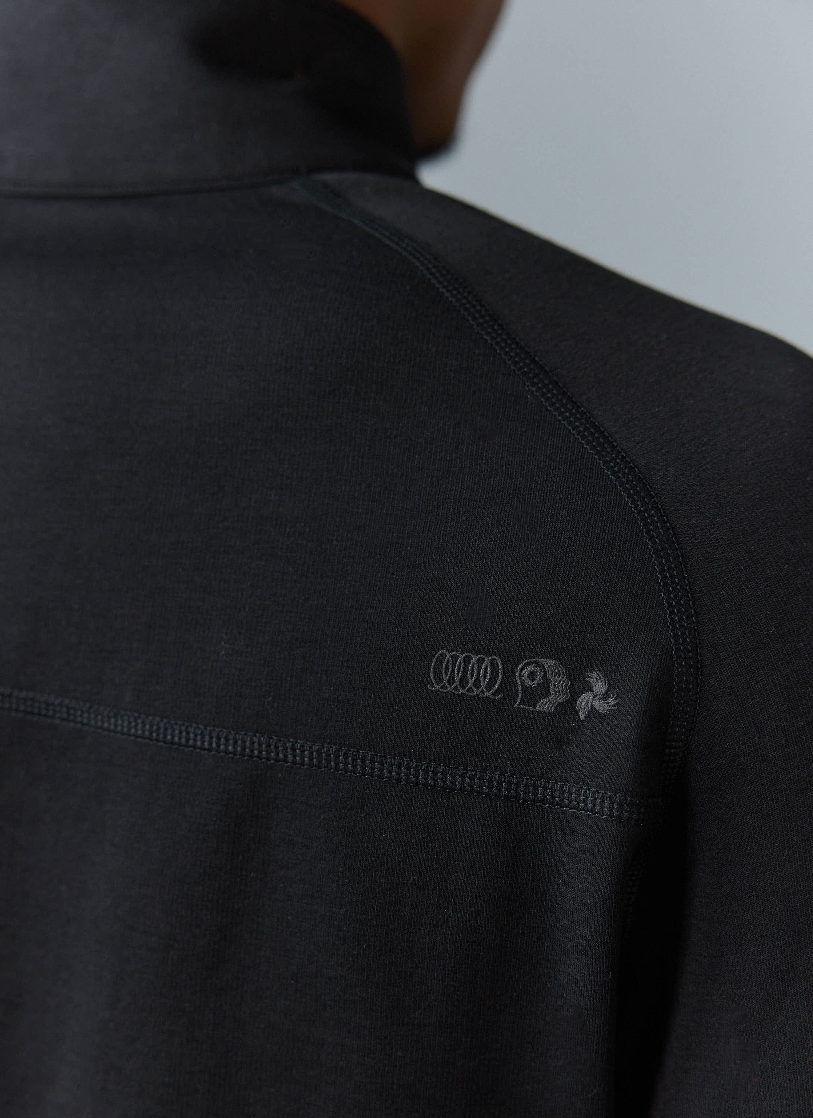 Close-up of the Percival PCVL Base Layer Quarter Zip in black, showing the tonal chest logo and flatlock seam detail.