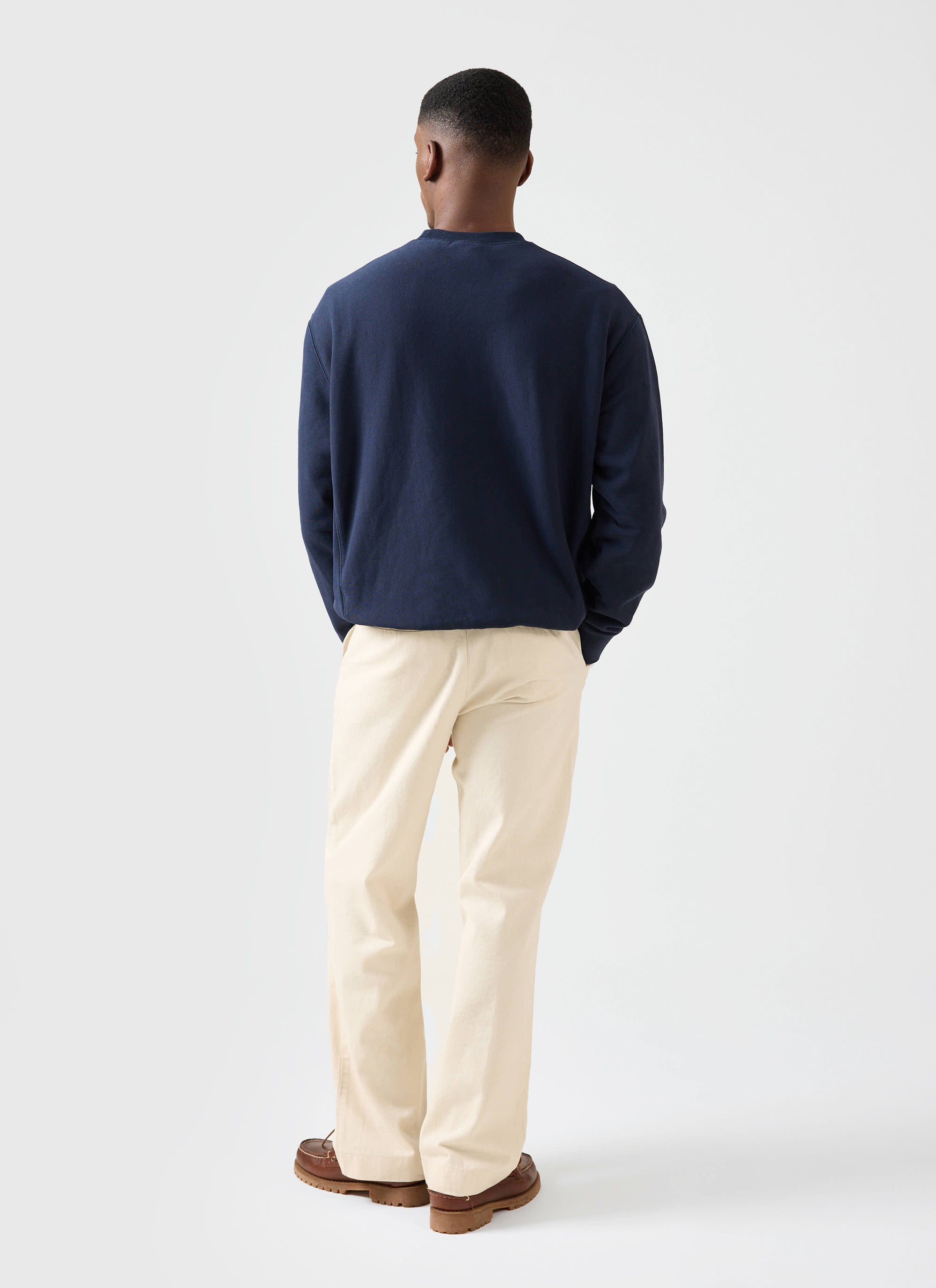 A man models the navy Champion x Percival Chenille Patch sweatshirt from behind, paired with cream trousers.
