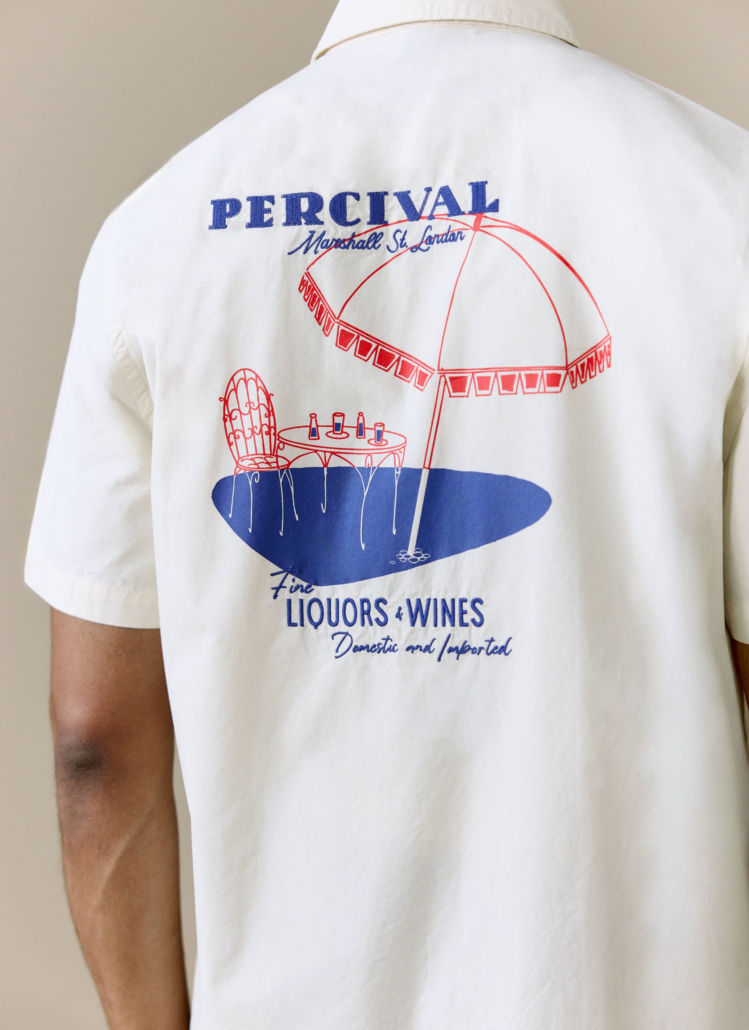 Close up on the back of a model wearing the Percival Harlow Boxy Shirt in ecru, showing the 'Fine Liquors & Wines' print.