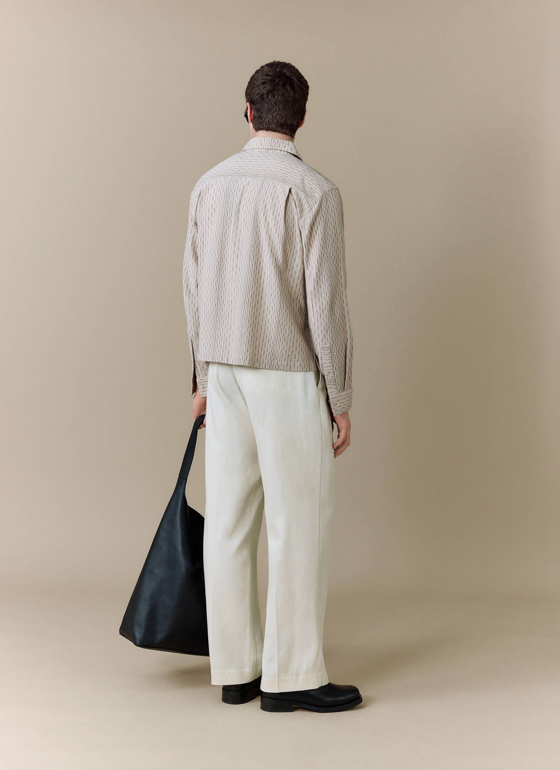 A model, shot from behind, wears the Percival Leland Cuban Boxy Shirt in ecru, styled with wide-leg trousers.
