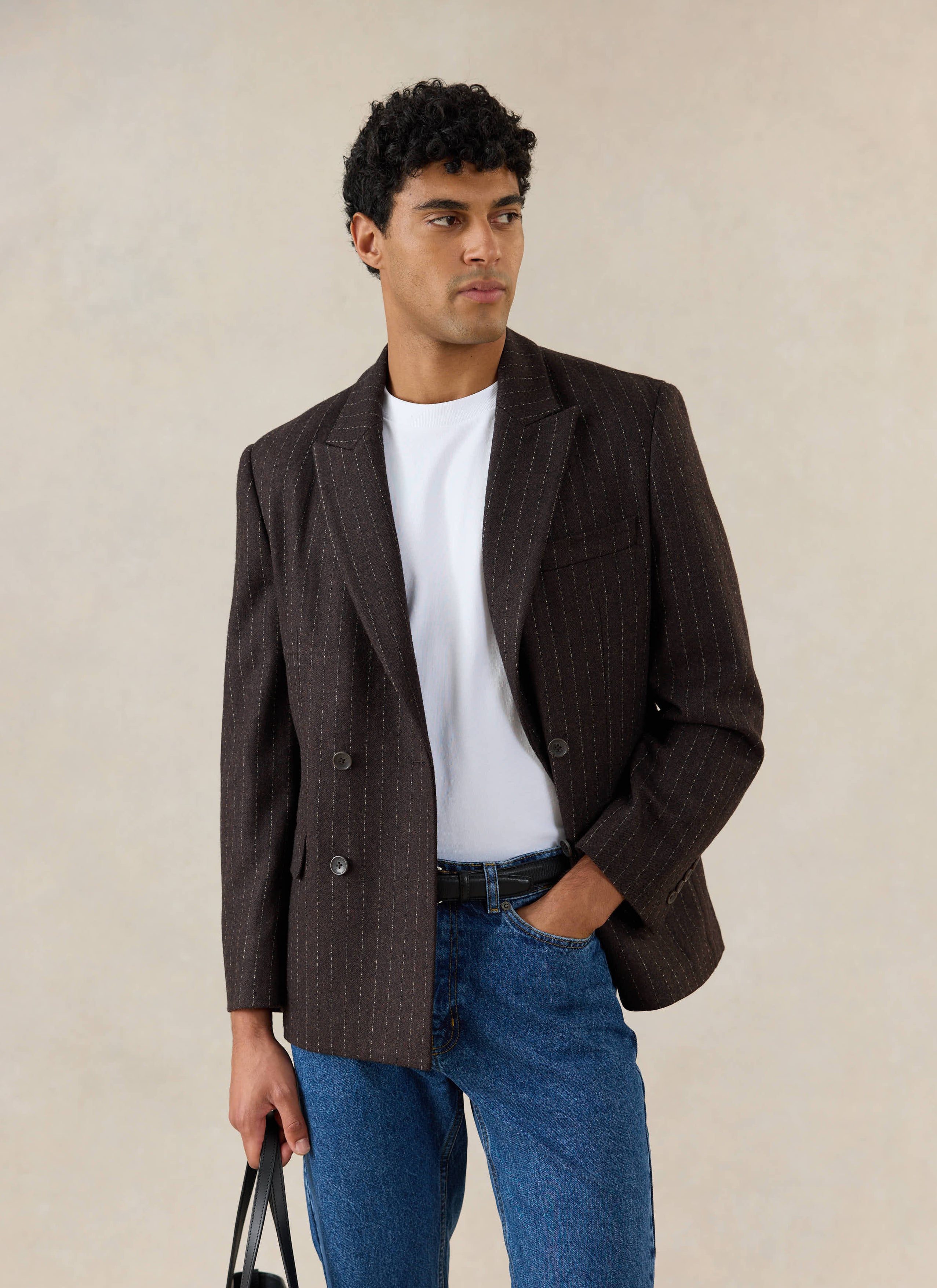 A model wears the Percival Clifton Pinstripe Double Breasted Blazer in espresso wool, with a white t-shirt and blue jeans.
