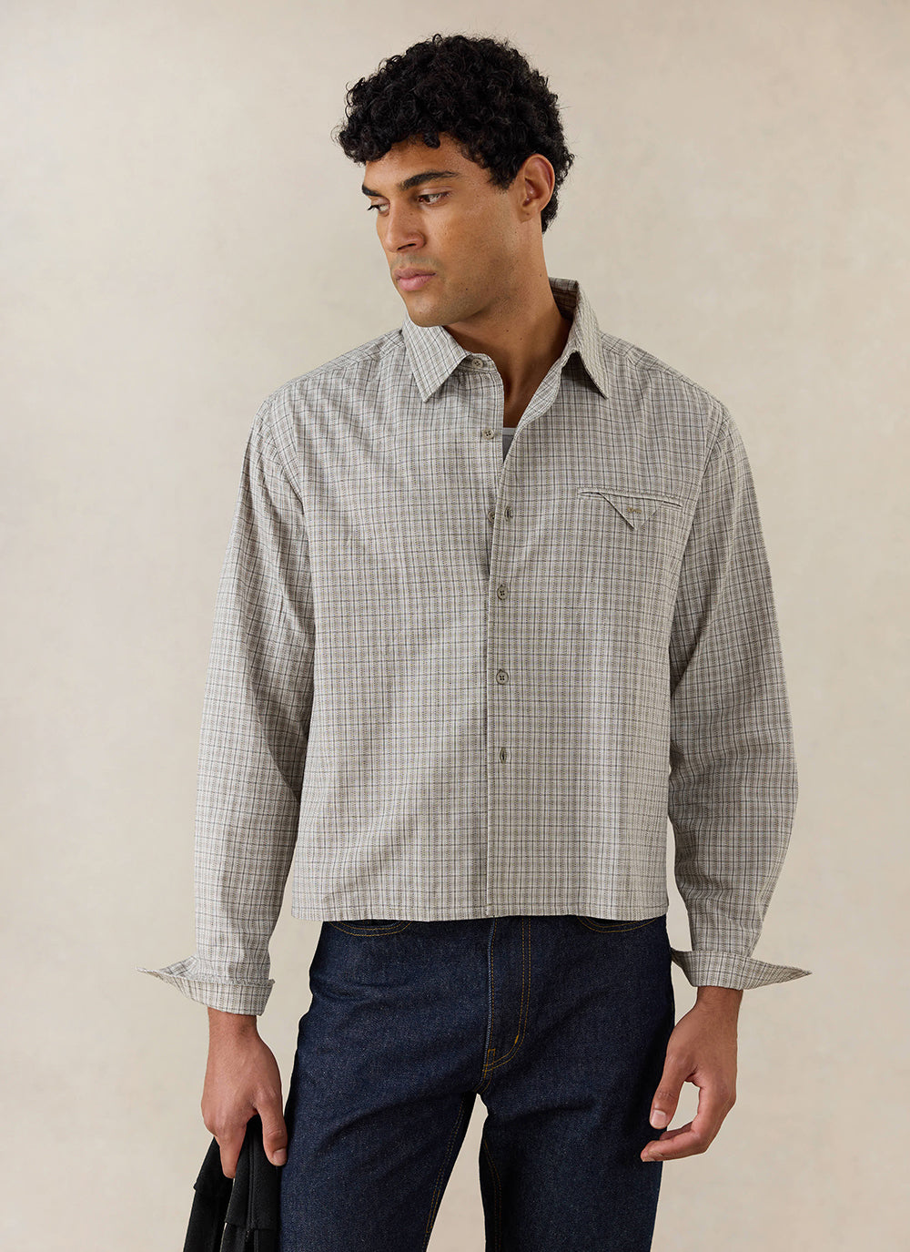 A model wears the cream check Percival Hinsley boxy long sleeve shirt, styled with dark blue denim jeans.