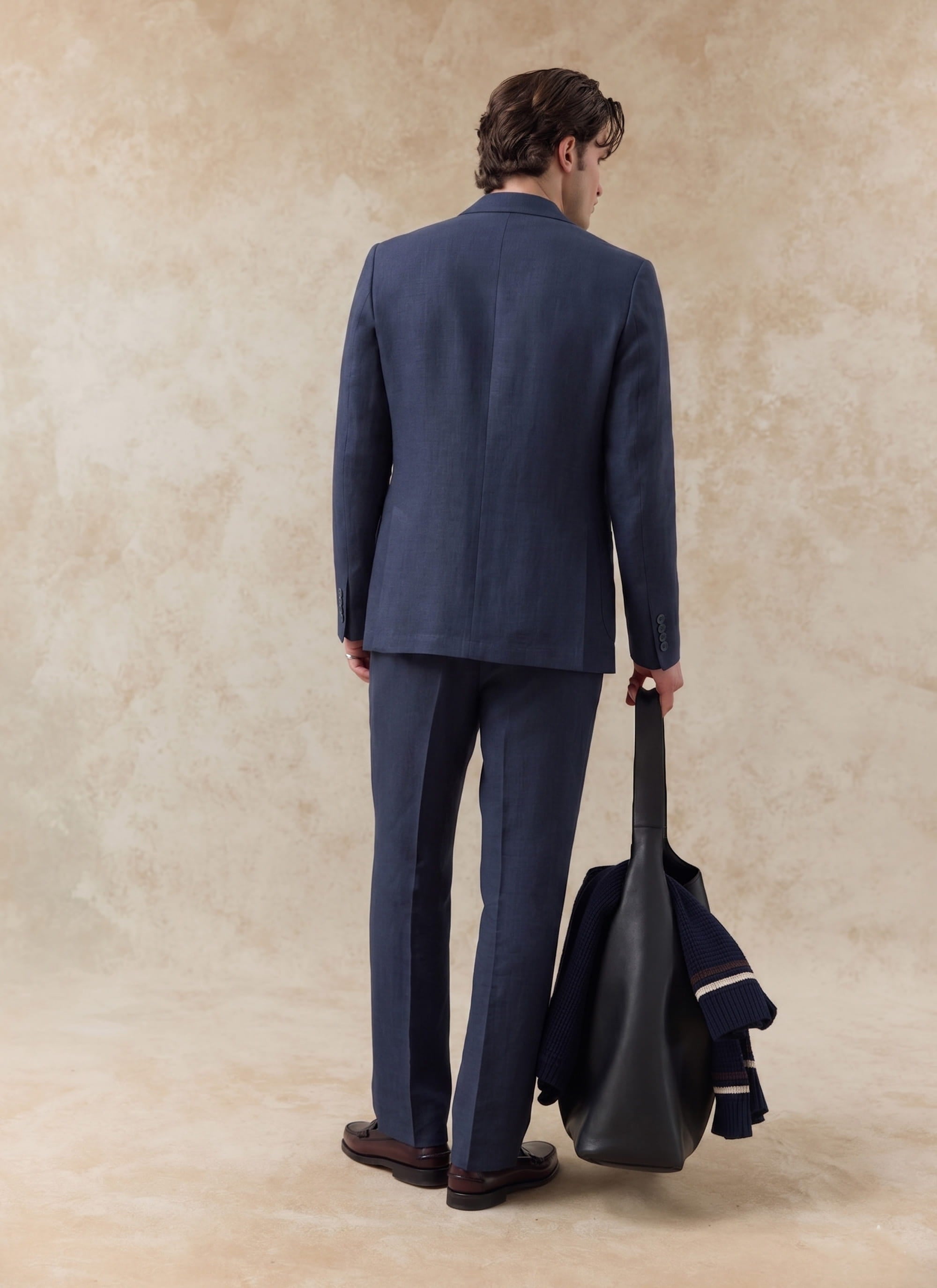 Rear view of the Percival navy tailored linen trousers and matching suit blazer, styled with a black leather bag.
