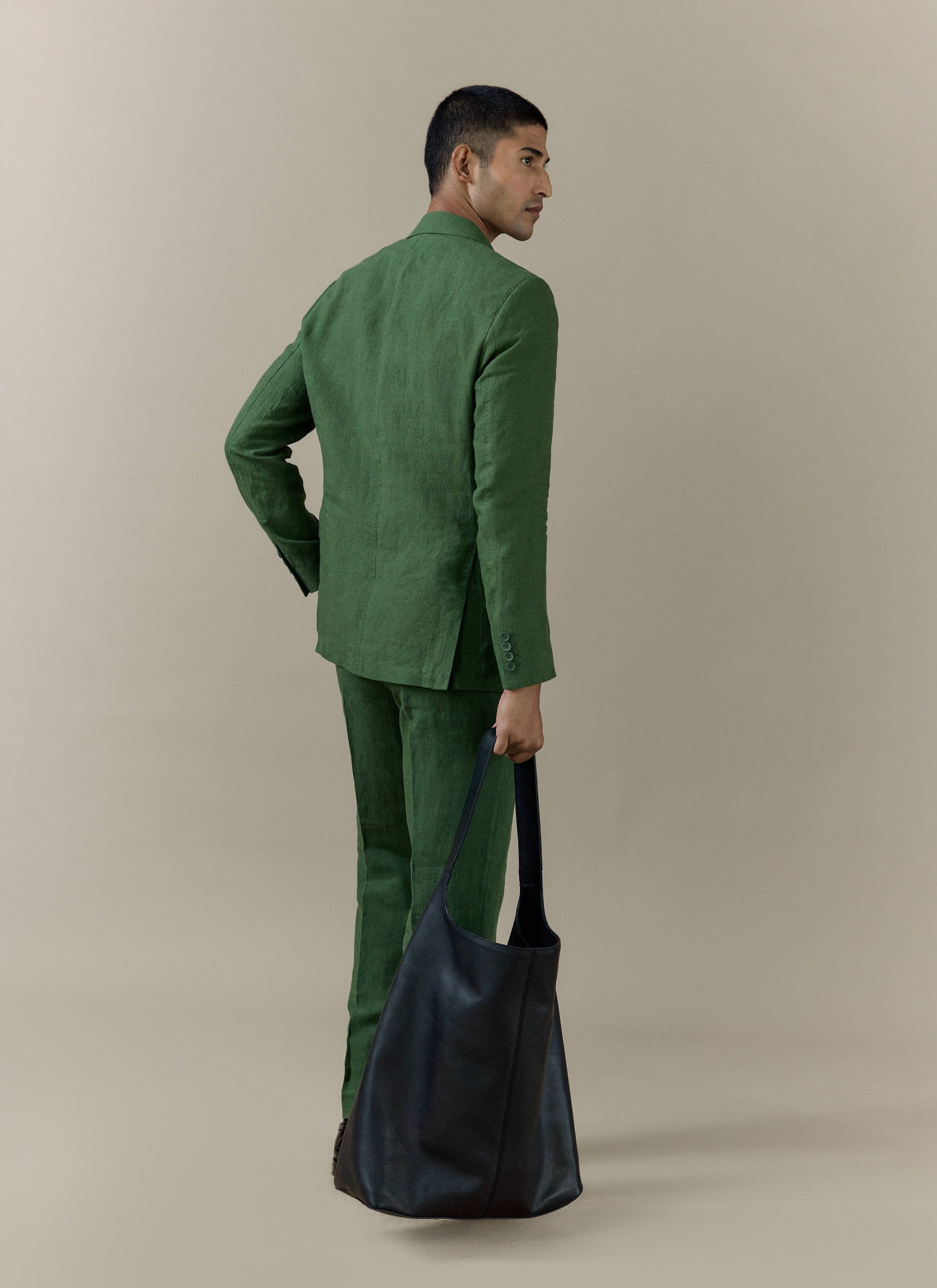 Rear view of the Percival slim fit classic blazer and trousers in forest green linen, paired with a large black bag.