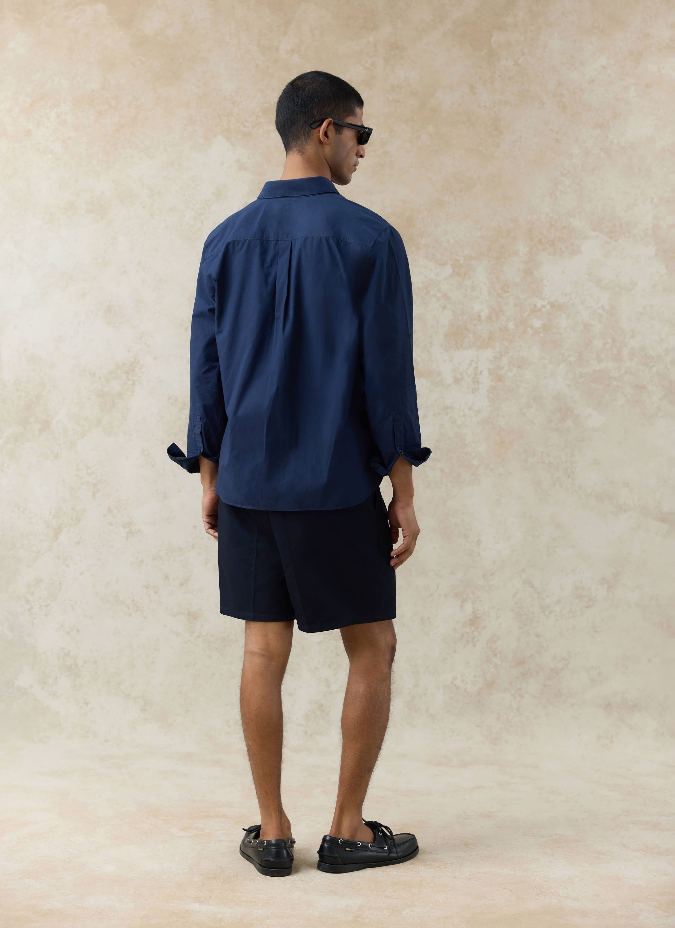 Back view of the navy cotton Dali Relaxed Poplin Shirt by Percival, featuring a back yoke and box pleat.
