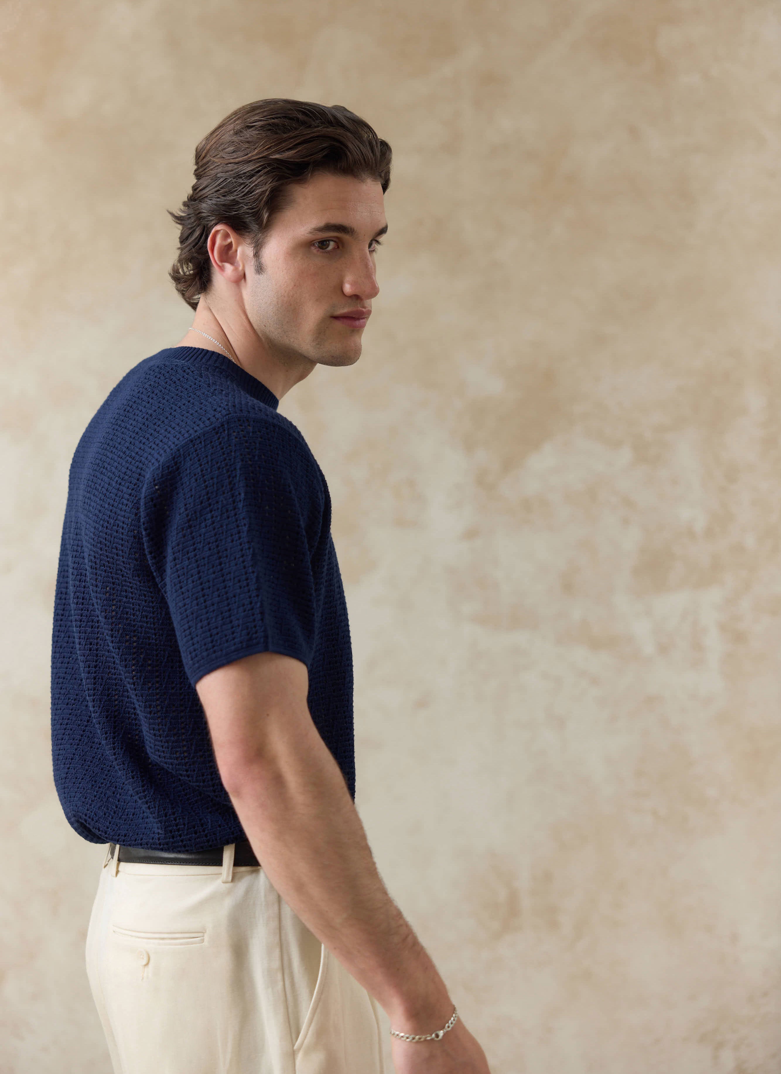 Navy Percival Siena Knitted T Shirt in a textured cotton open-work, styled with cream trousers on a model in profile.