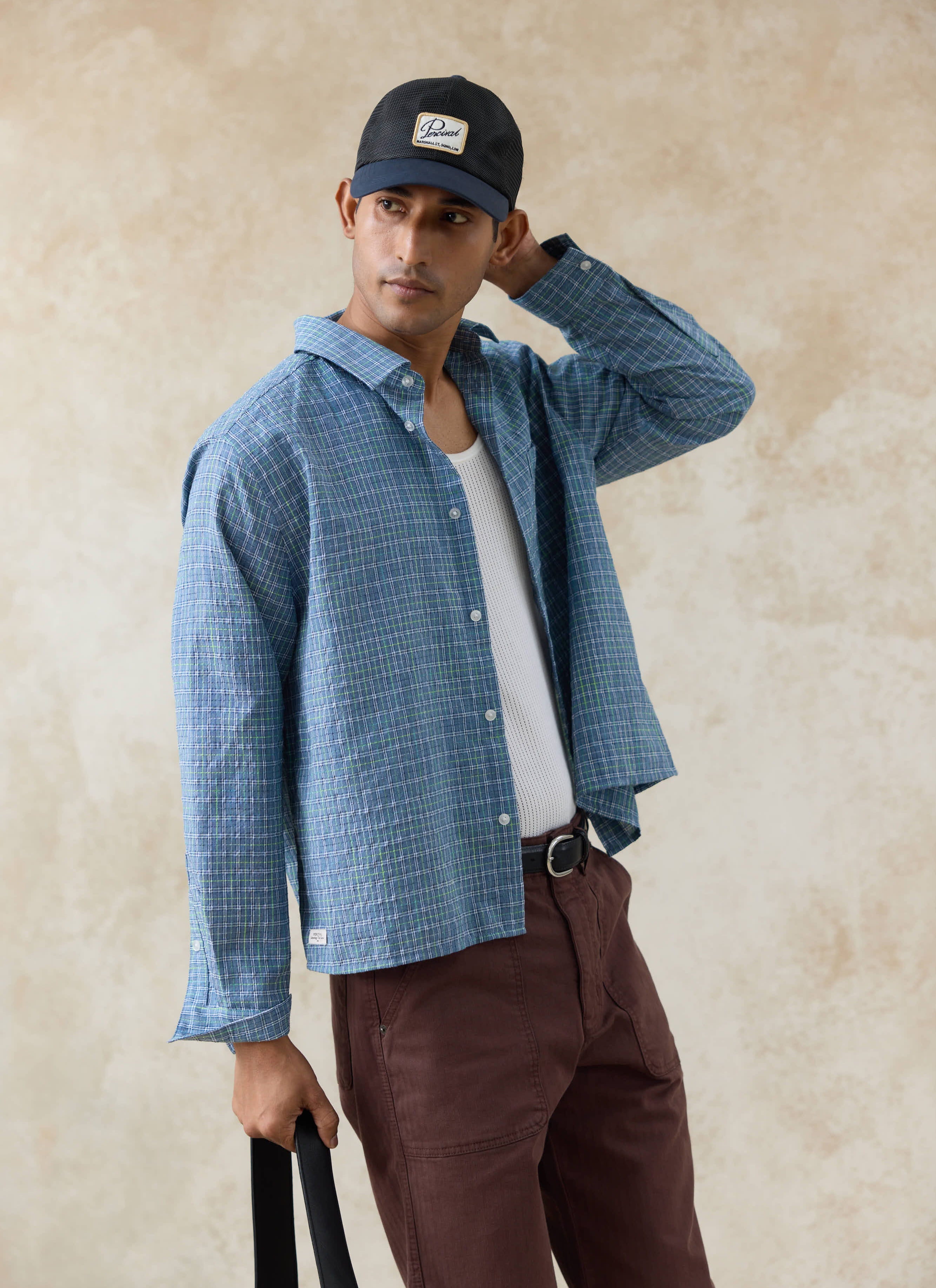 Model wearing the blue Percival Hinsley Checked Boxy Shirt in cotton grid, styled open over a white mesh vest.