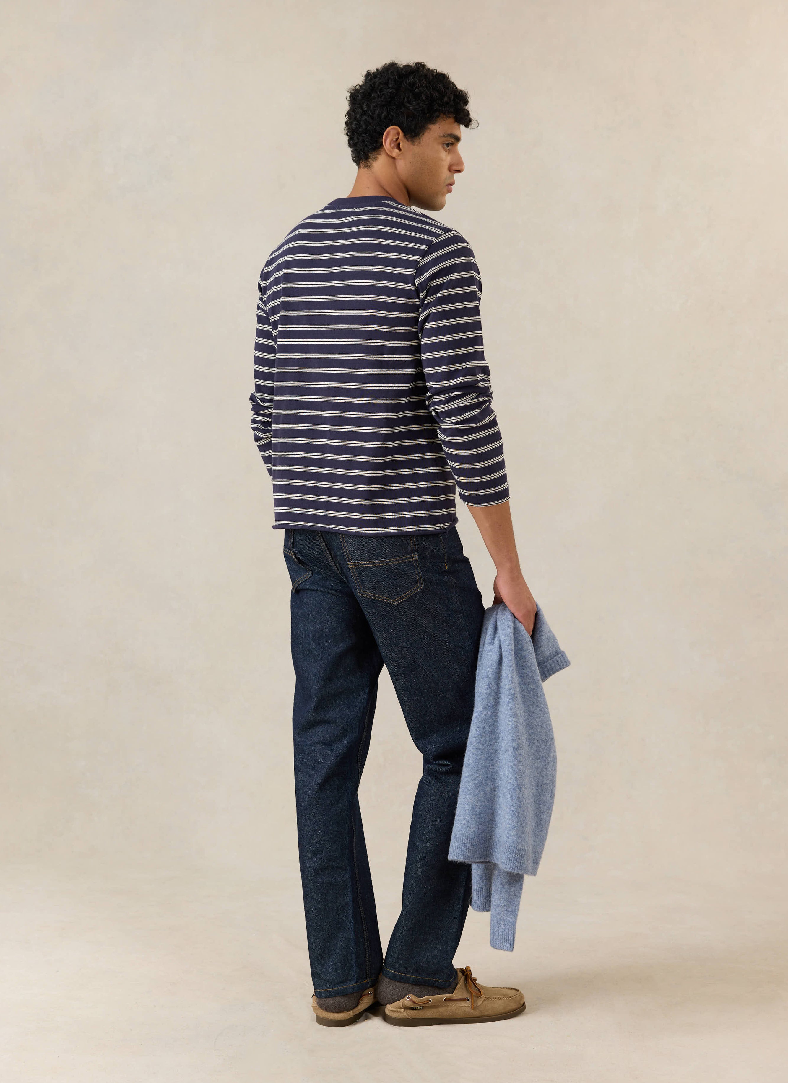 A model wears the navy stripe Percival Arlo Breton long sleeve t-shirt, styled with dark denim jeans in a studio.