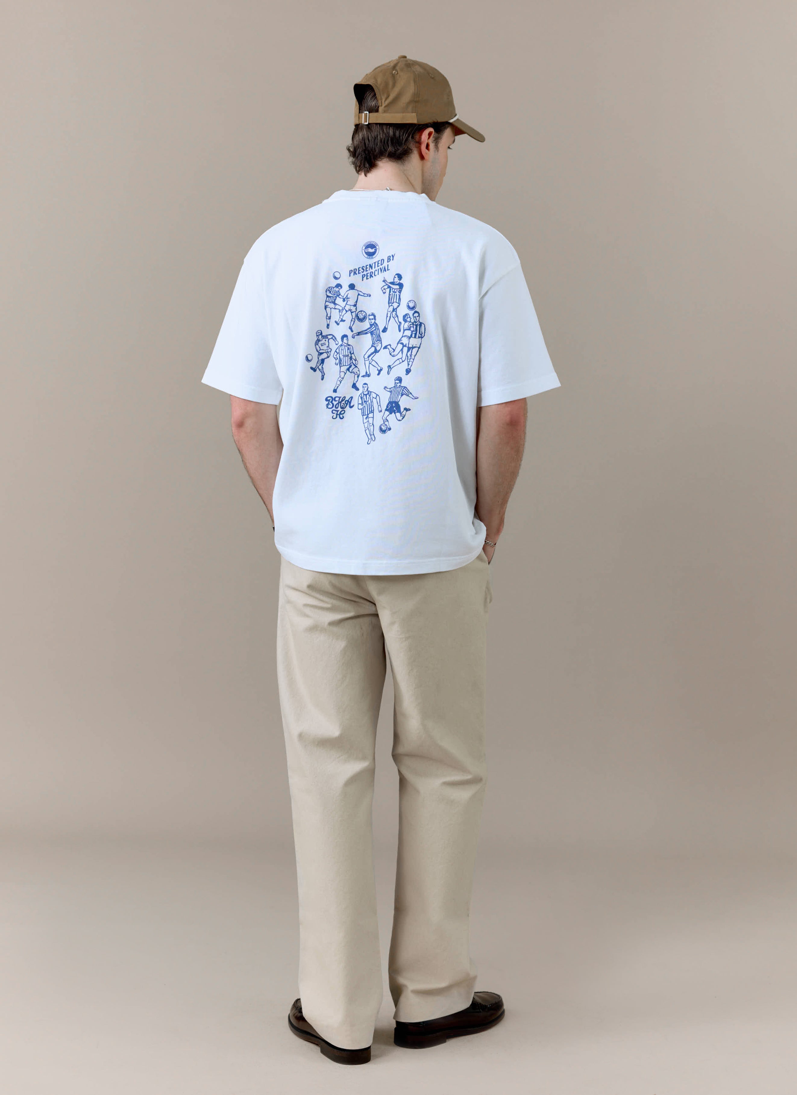 A model wears the white Percival x Brighton & Hove Albion F.C. t-shirt, showing the blue football graphic on the back.