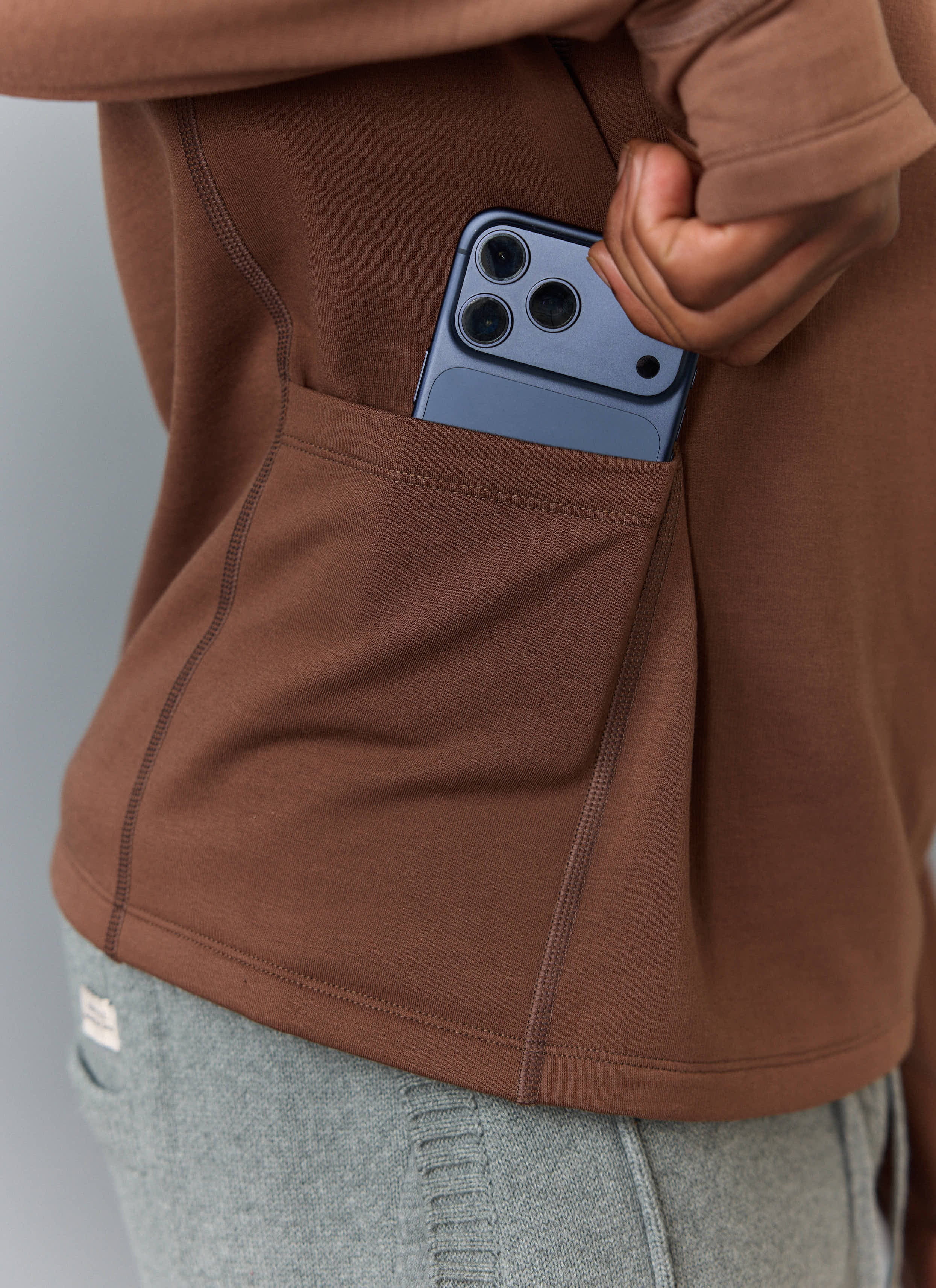 A close-up of the side stash pocket on the Percival PCVL Base Layer Quarter Zip in rust, showing a phone fitting inside.