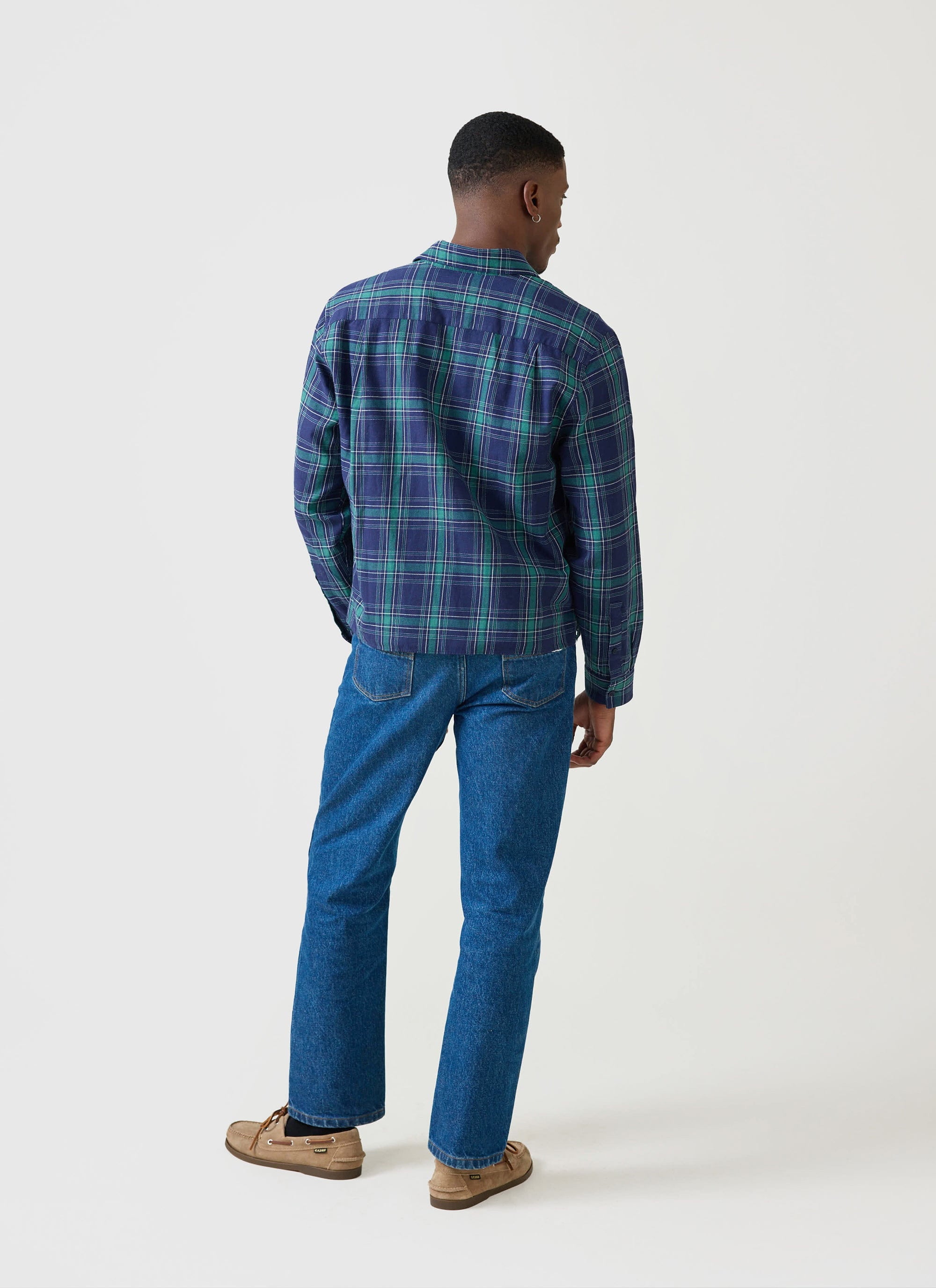Rear view of a model wearing the Percival x Champion check boxy shirt in blue and green, styled with denim jeans.