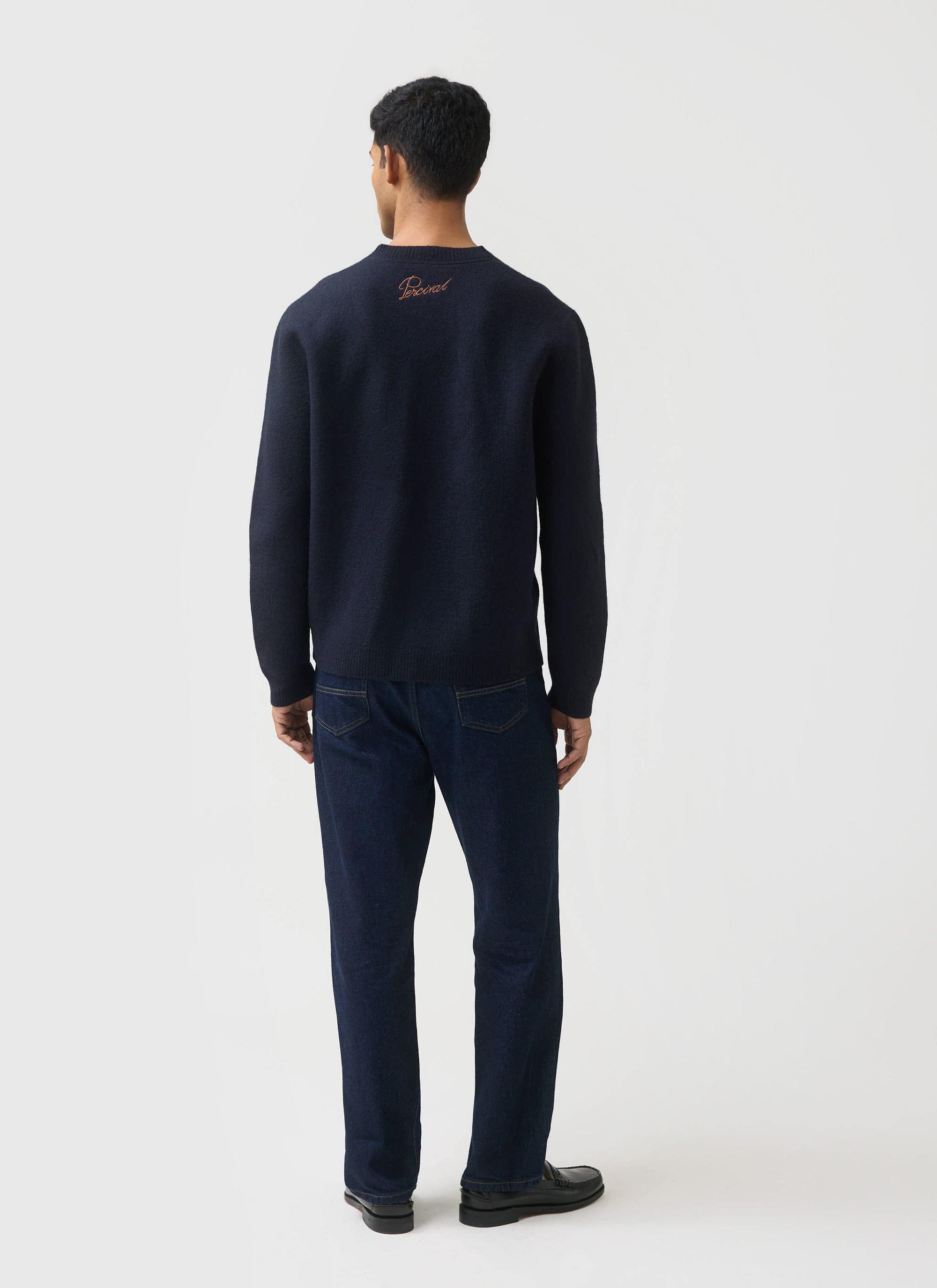 A model wears the navy Guinness x Percival merino wool jumper, showing the embroidered Percival logo on the back.