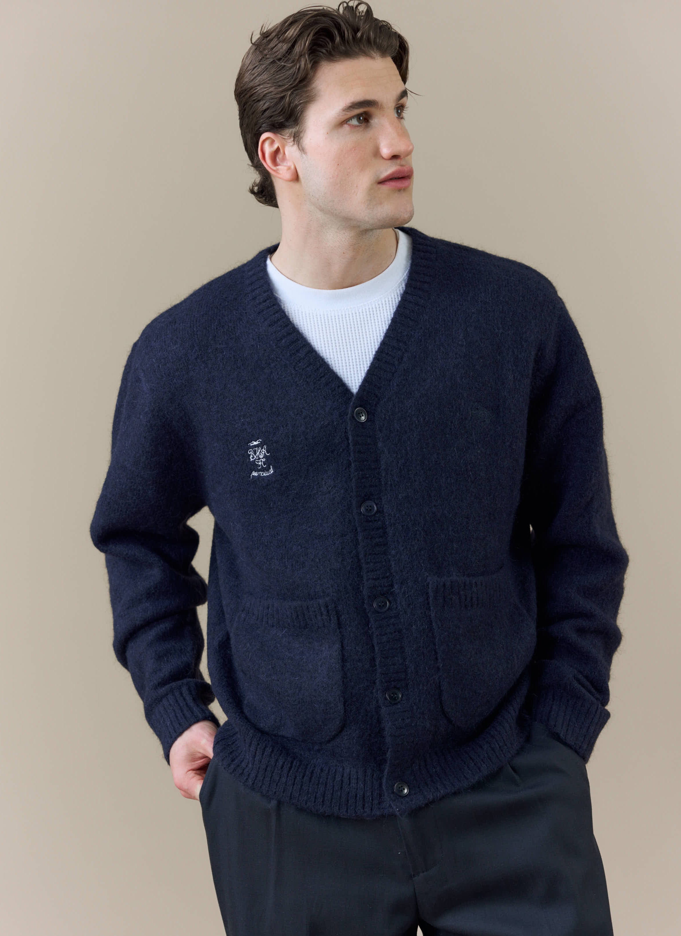 A model wears the Percival x Brighton & Hove Albion F.C. White Glove Cardigan in navy, showing the collaborative embroidery.